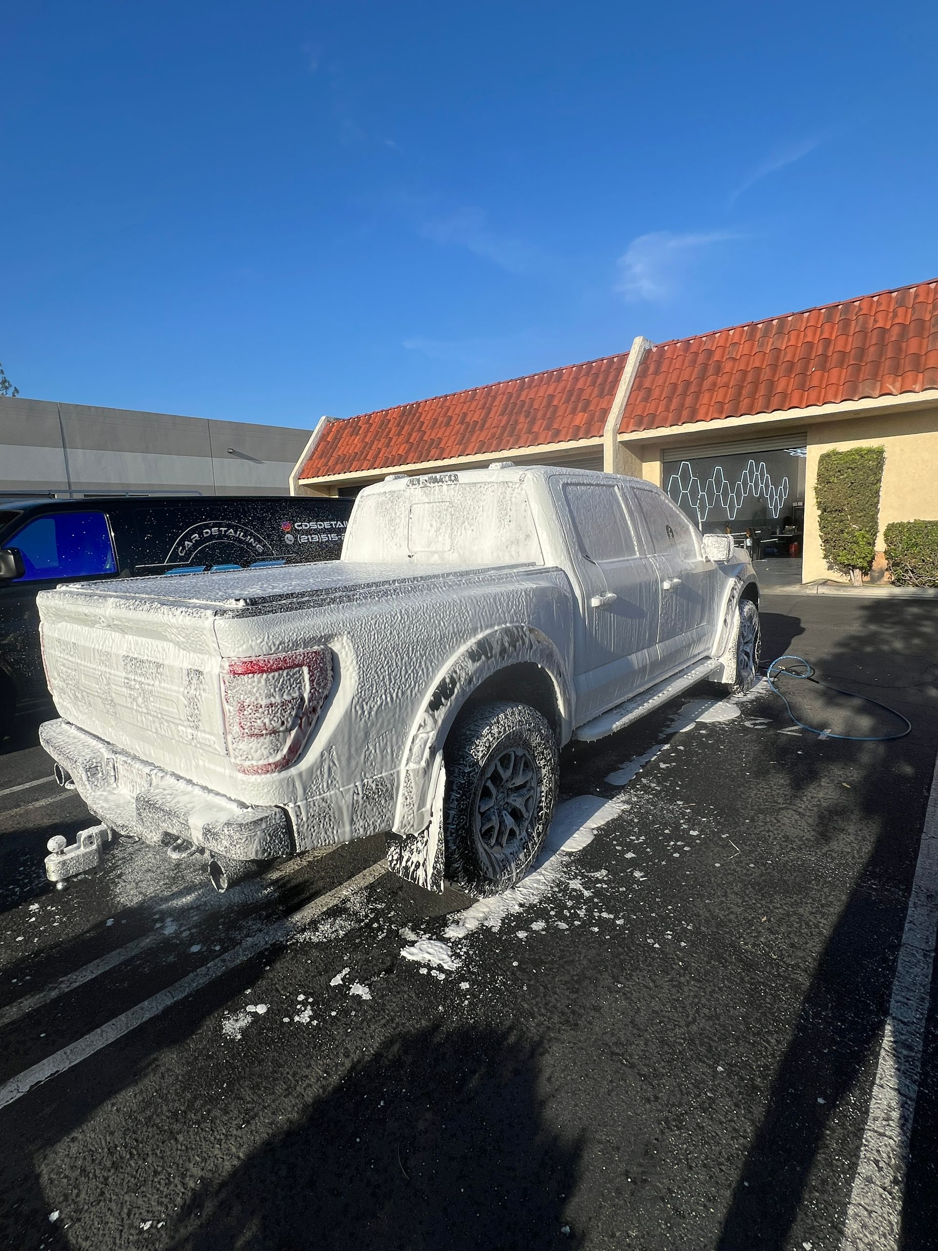 White pickup truck covered in foam at a car wash under a bright blue sky