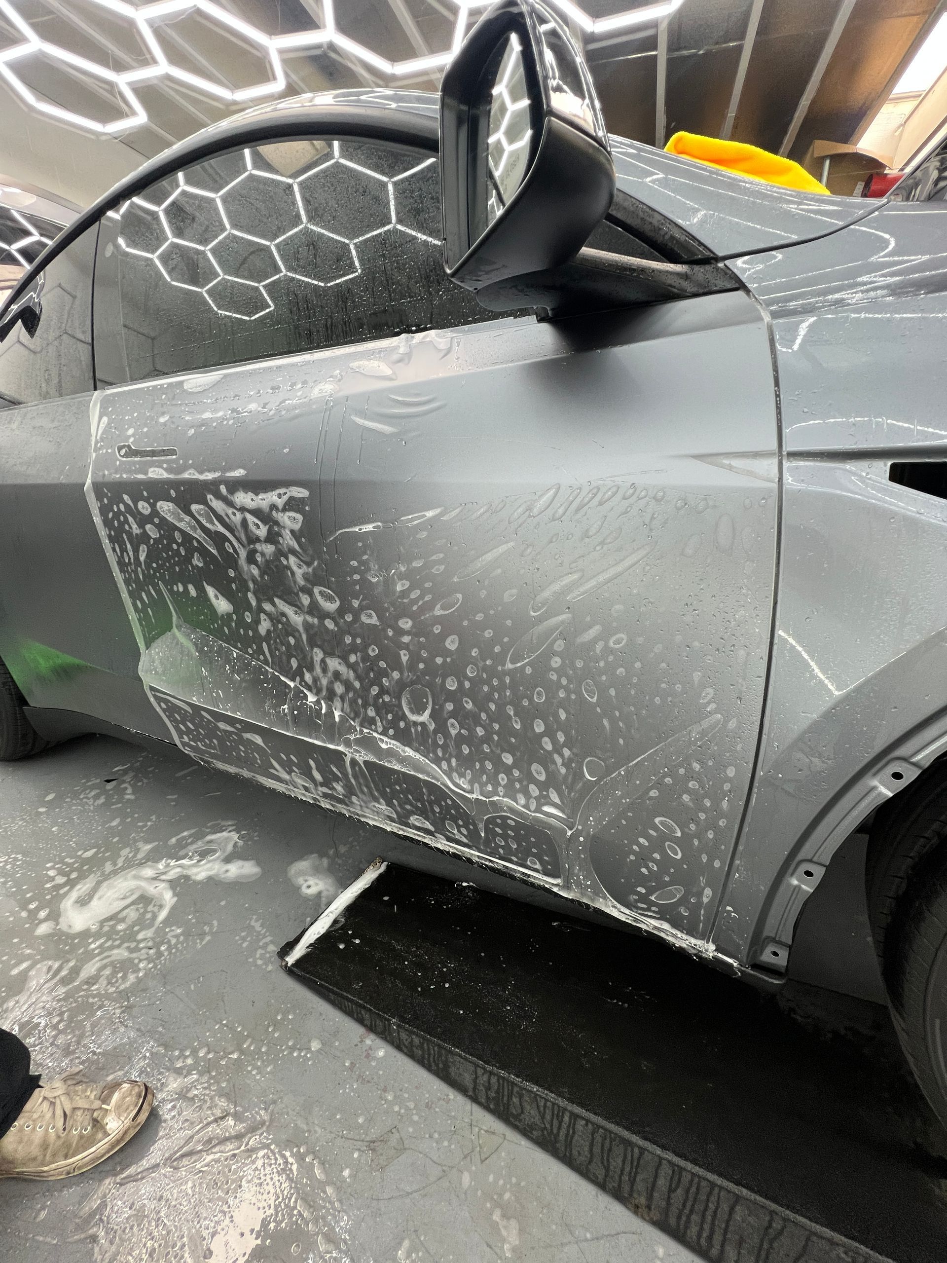 Gray car with white foam or residue on the side at a car wash conveyor.