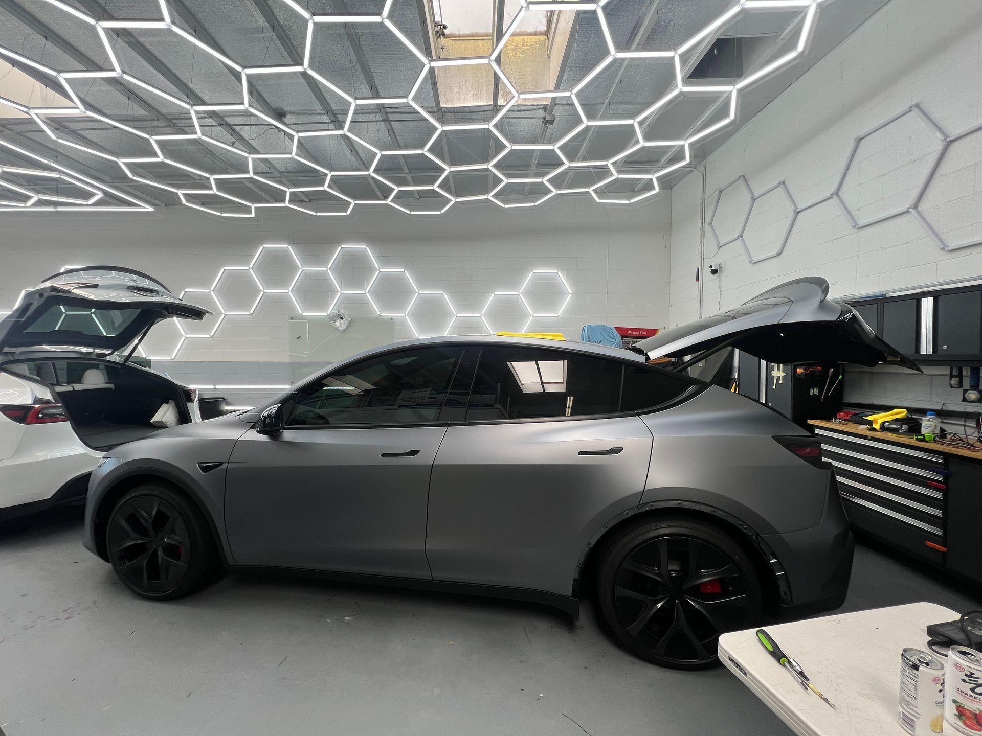 Gray sports car in a modern garage with geometric ceiling lights and open rear hatch and trunk