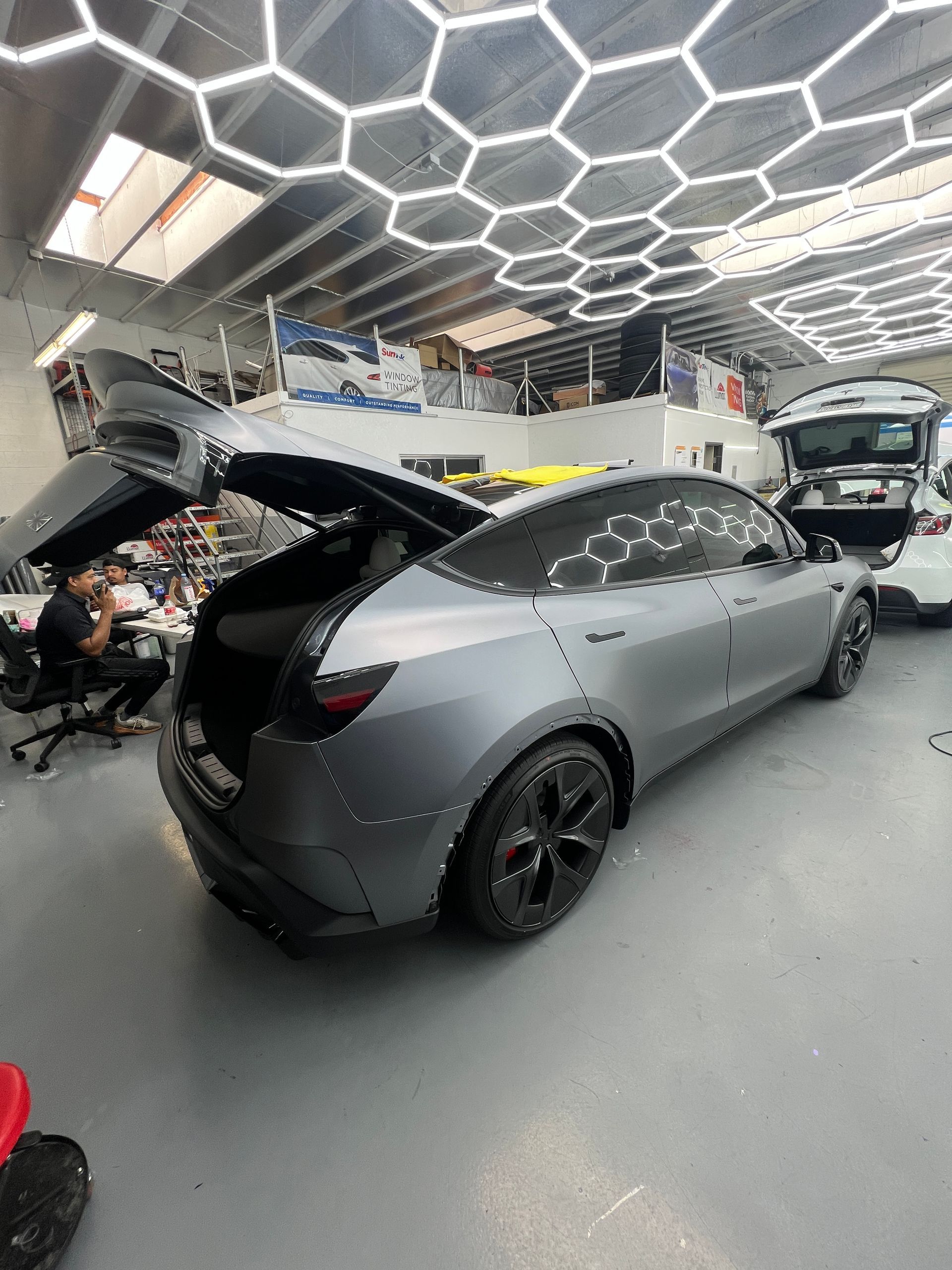 Gray hatchback with open rear hatch in a modern garage showroom, with another car and a motorcycle nearby