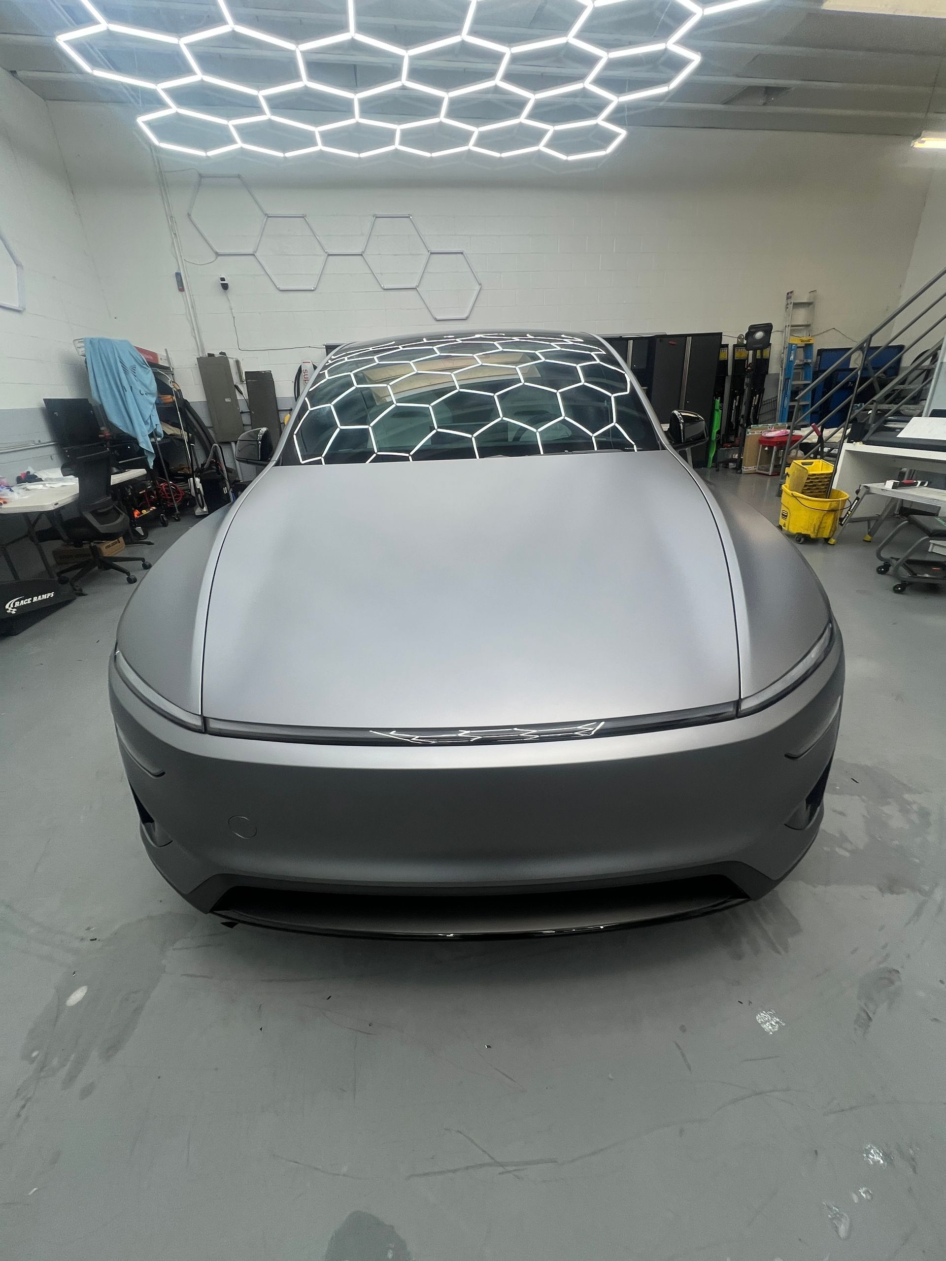 Front view of a silver car covered indoors in a workshop with hexagonal ceiling lights