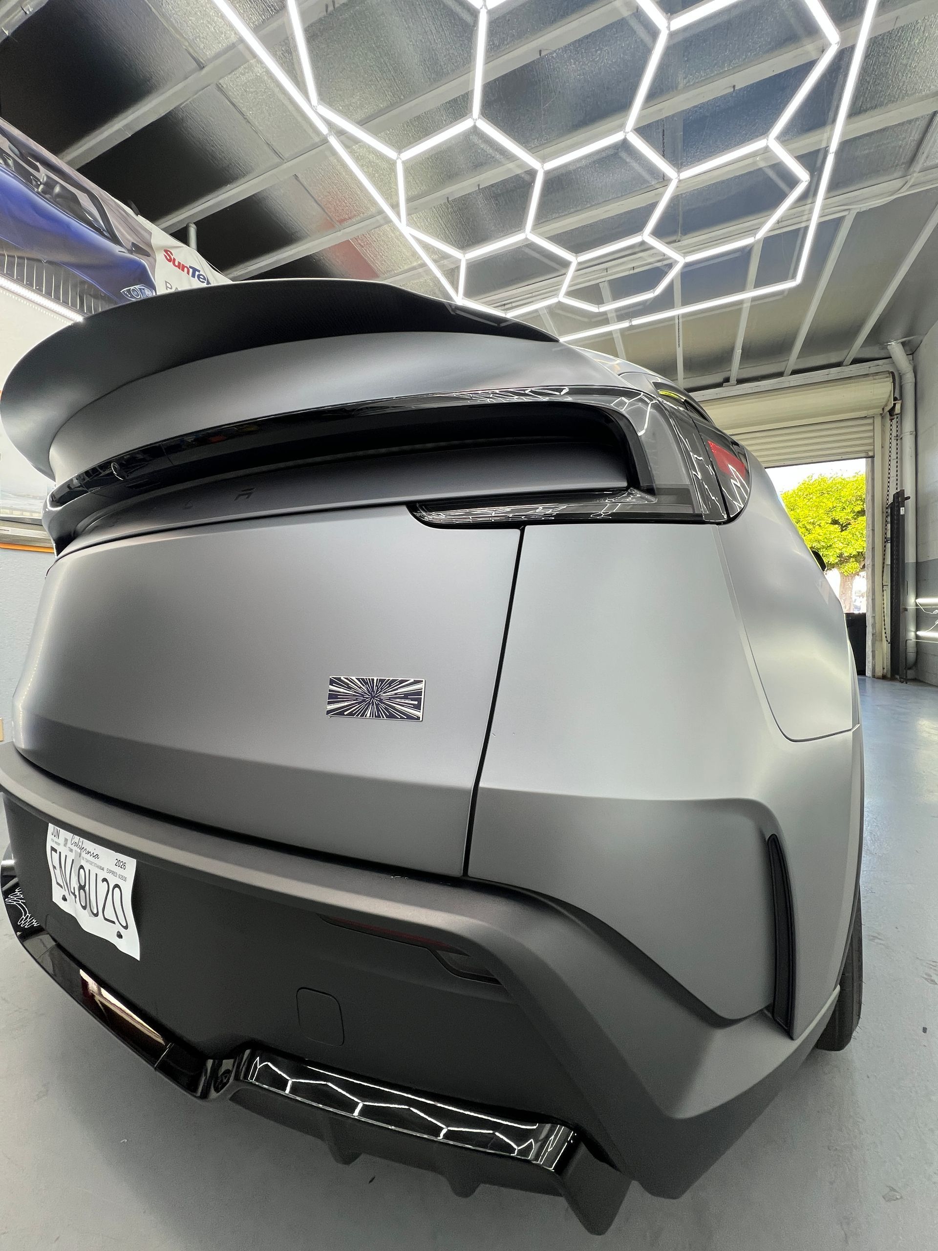 Rear view of a matte gray SUV with a black roof box parked under a modern carport