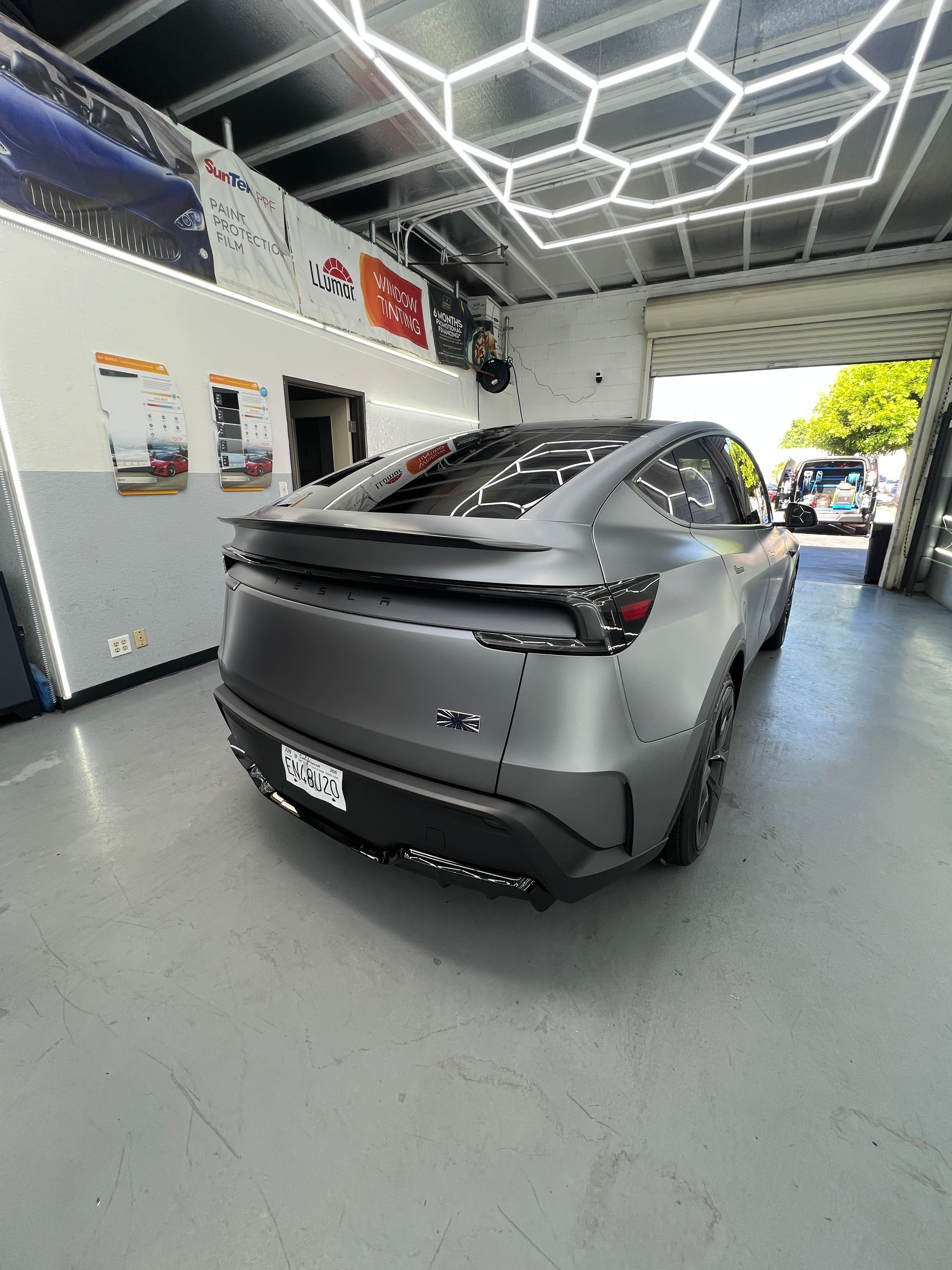 Matte gray sports car in a showroom with hexagonal ceiling lights and wall displays