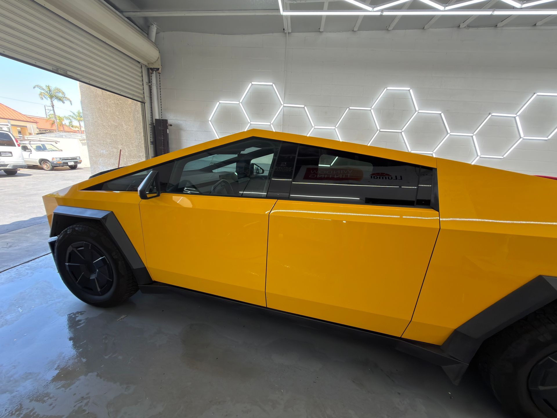 Yellow Cybertruck parked in a garage with hexagonal wall lights and a wet floor