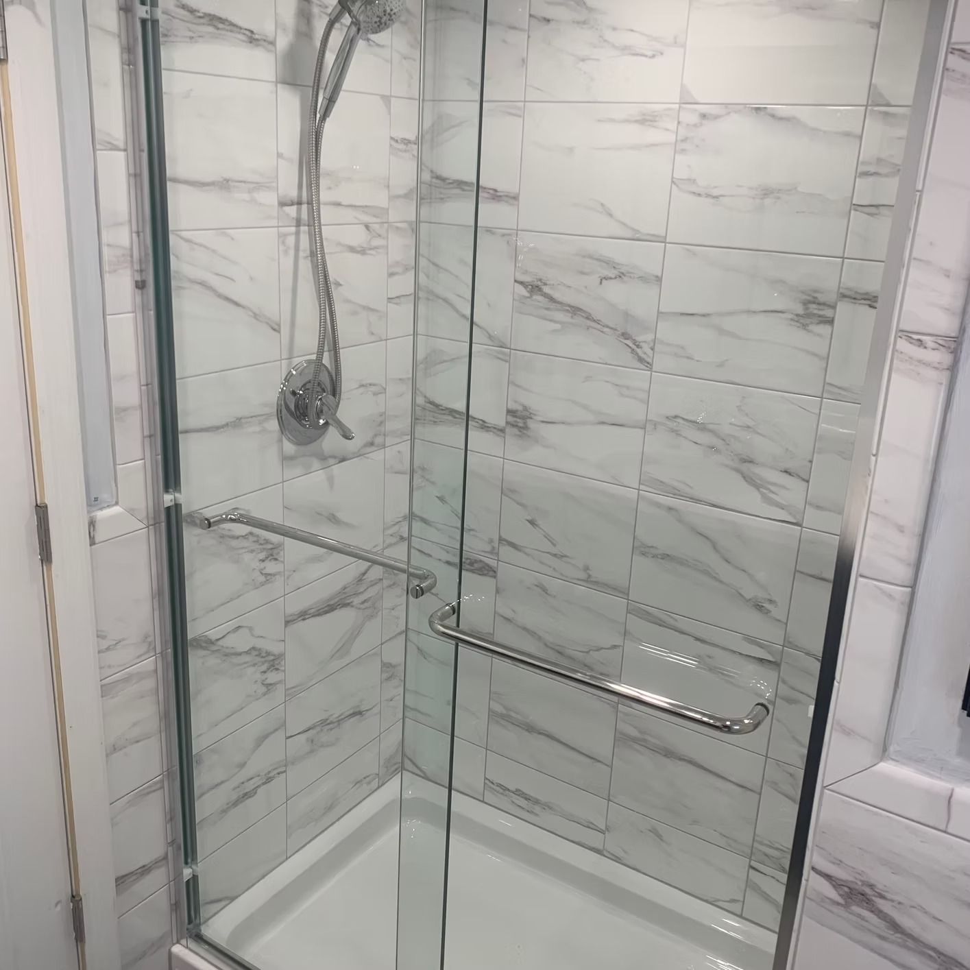 Shower stall with clear glass doors and marble-look tiles. Silver shower fixtures.