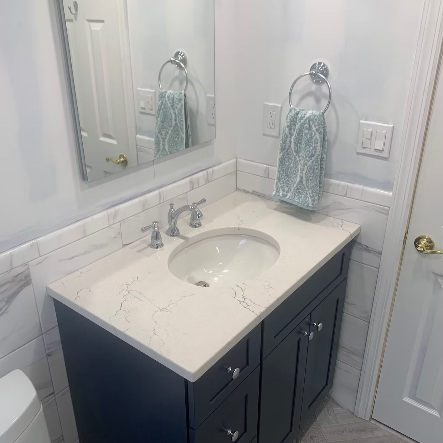 Bathroom with a white countertop, dark blue cabinet, oval sink, mirror, and a towel.