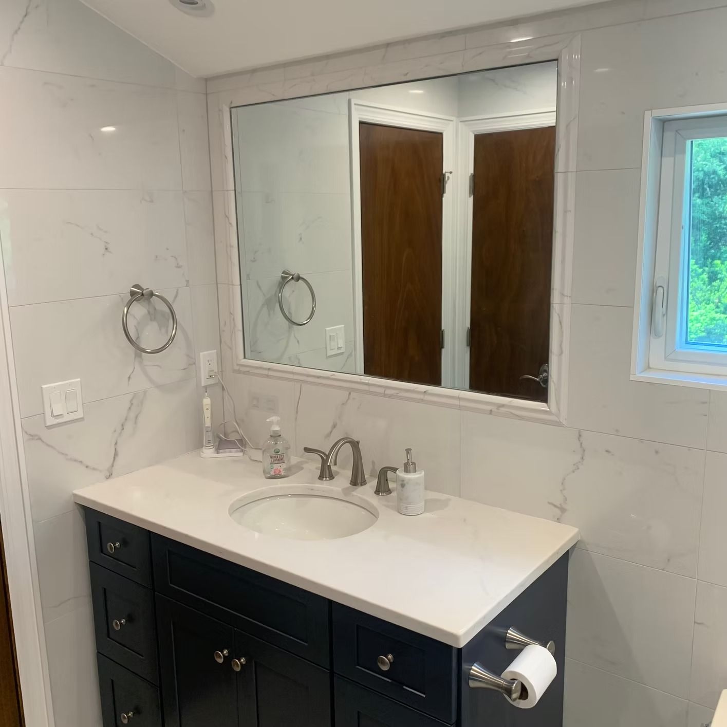 Bathroom with navy vanity, white countertop, large mirror, and white tile walls.