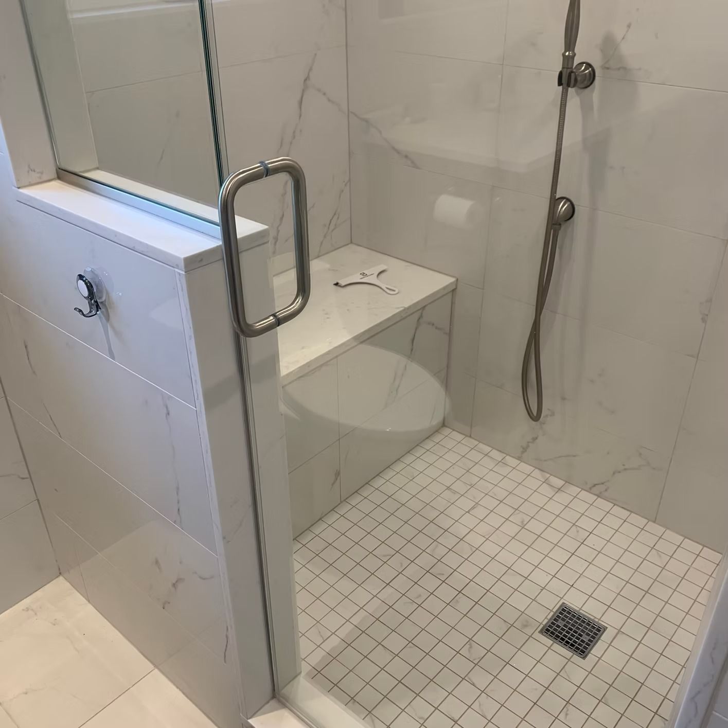 Accessible shower with white marble tile, a built-in seat, and glass door.