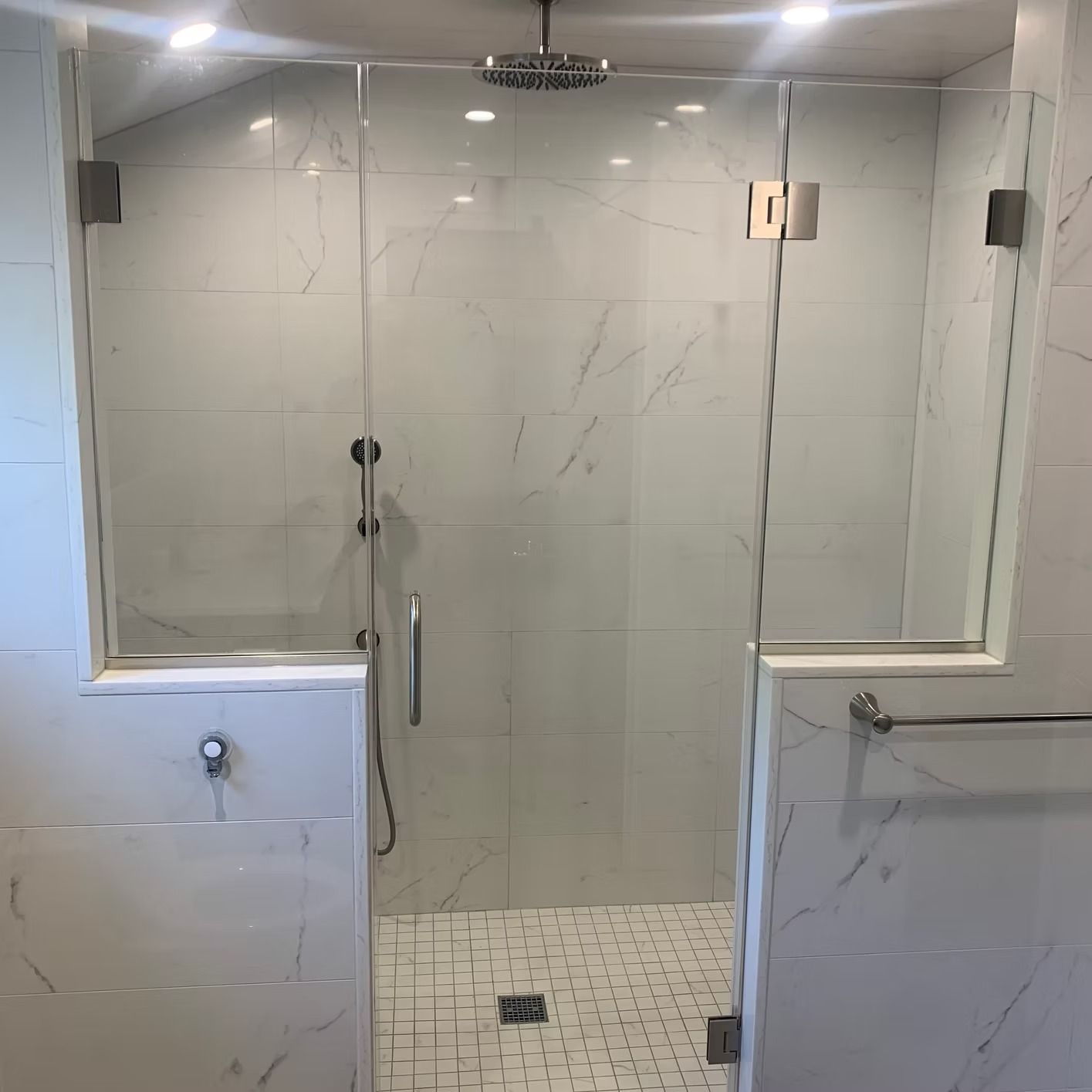 Glass shower enclosure with white marble-like tile walls and a mosaic tiled floor.