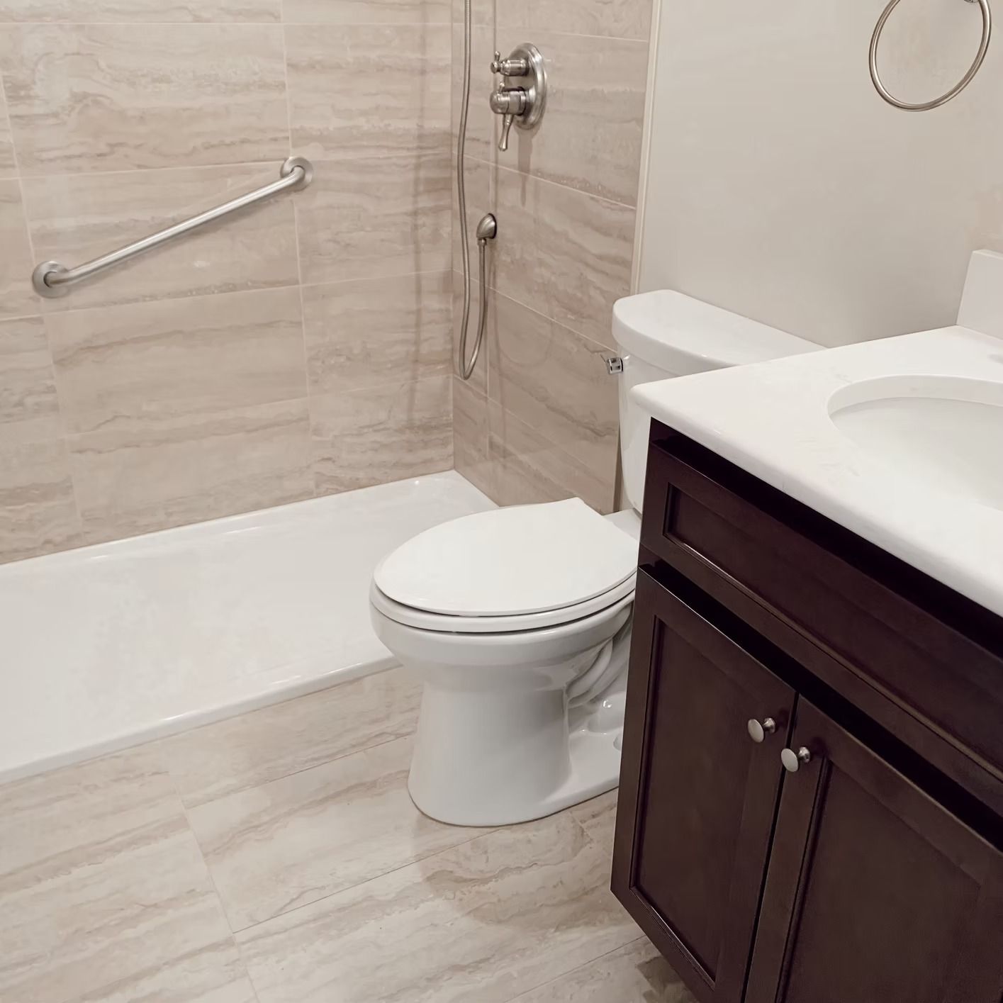 Bathroom with beige tile, white tub, toilet, dark brown vanity, and grab bar.