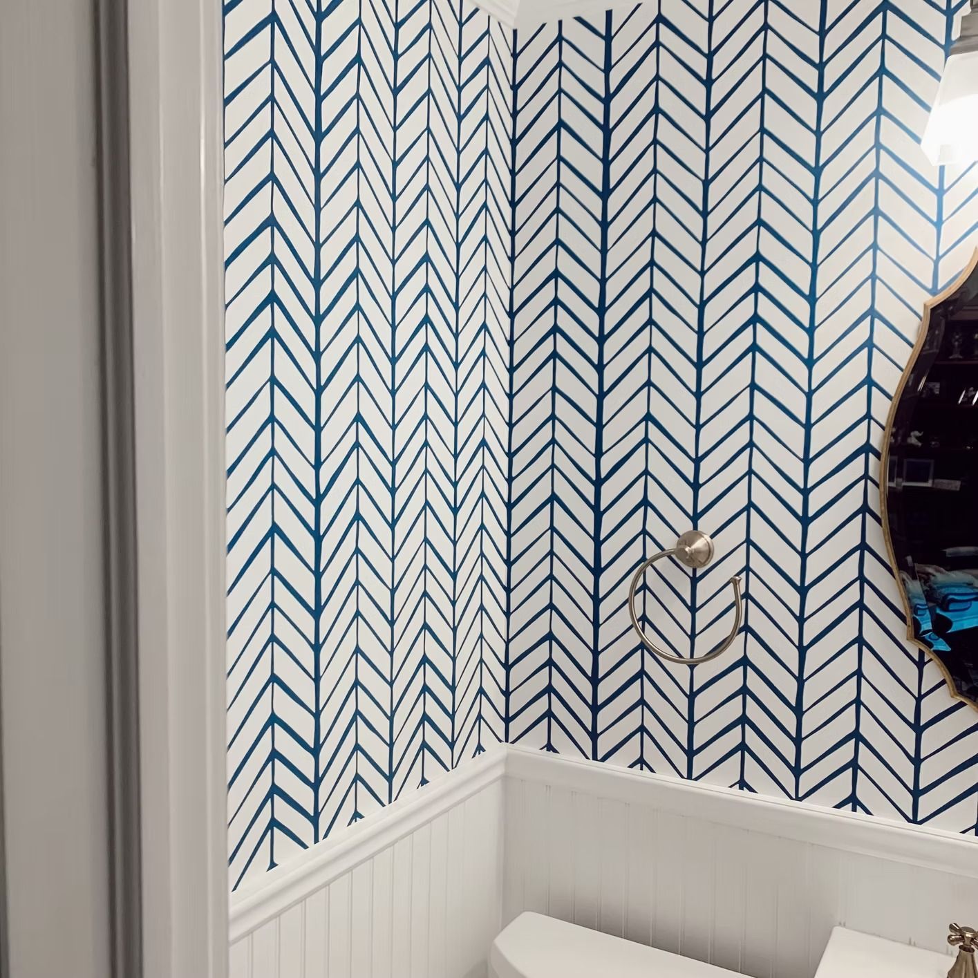 Bathroom with blue and white herringbone wallpaper, white trim, and a gold towel holder.