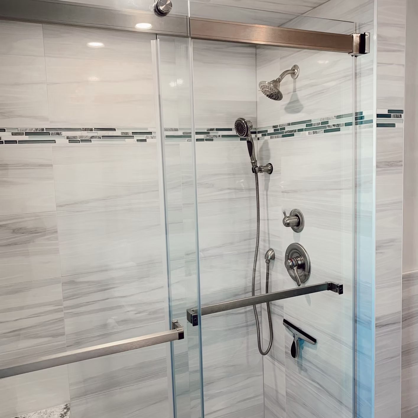 Glass shower enclosure with silver fixtures and white tiled walls.