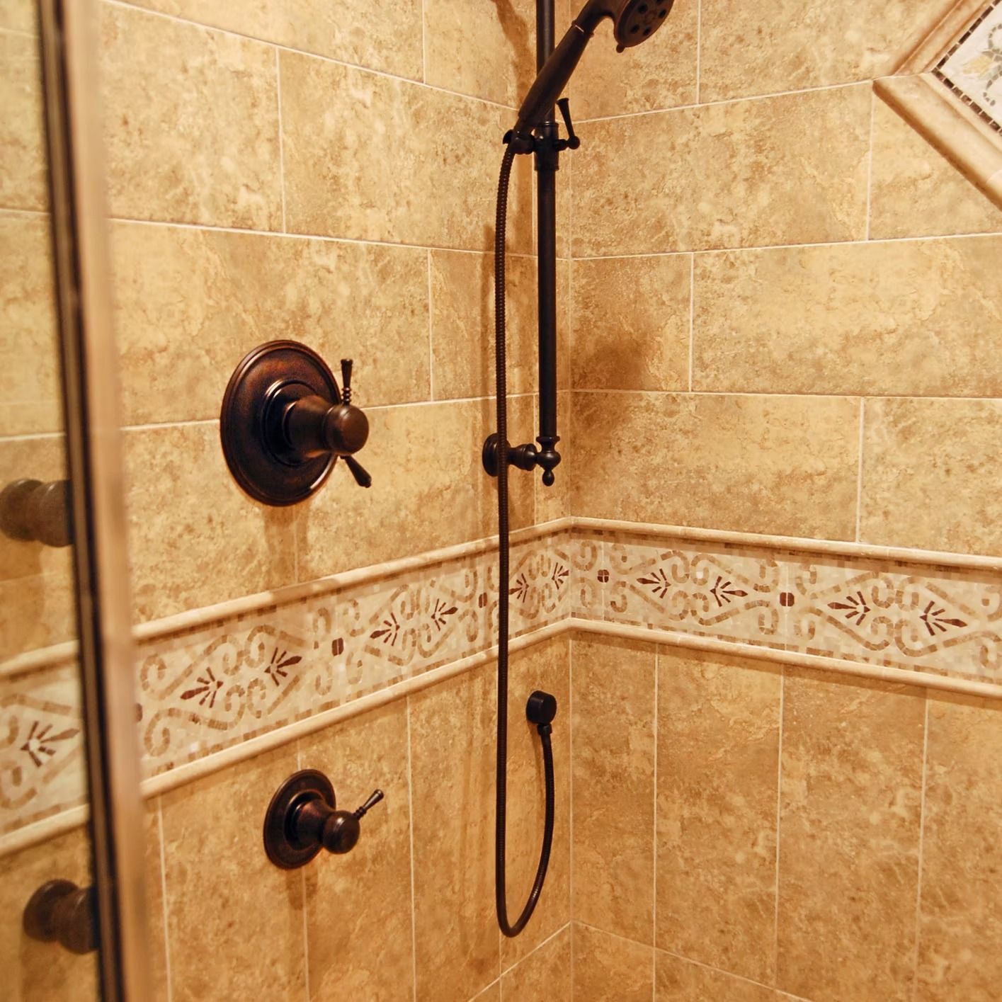 Shower interior with bronze fixtures, beige tiled walls, and decorative border.