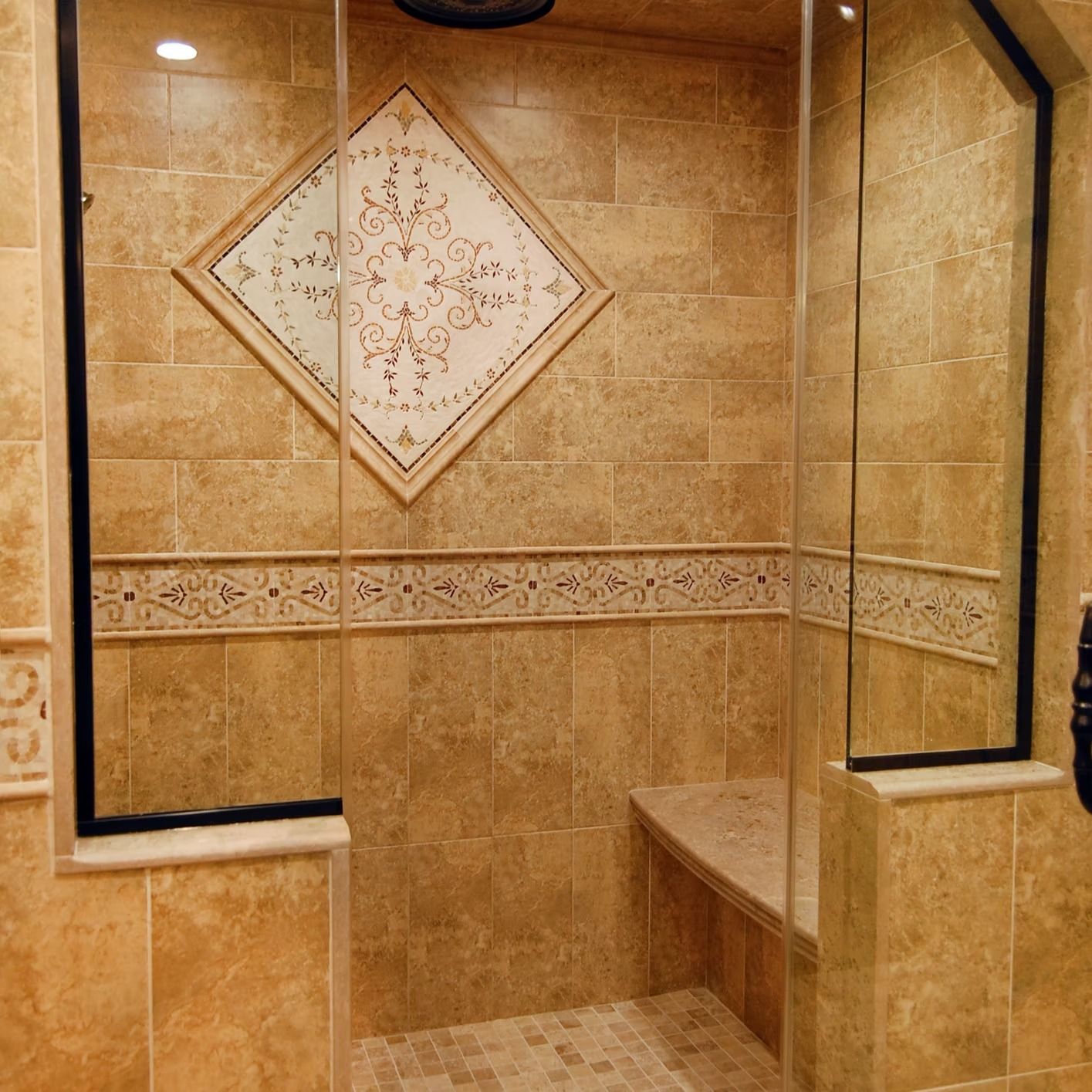Shower with tan tile, decorative tile border, a built-in bench, and glass door.