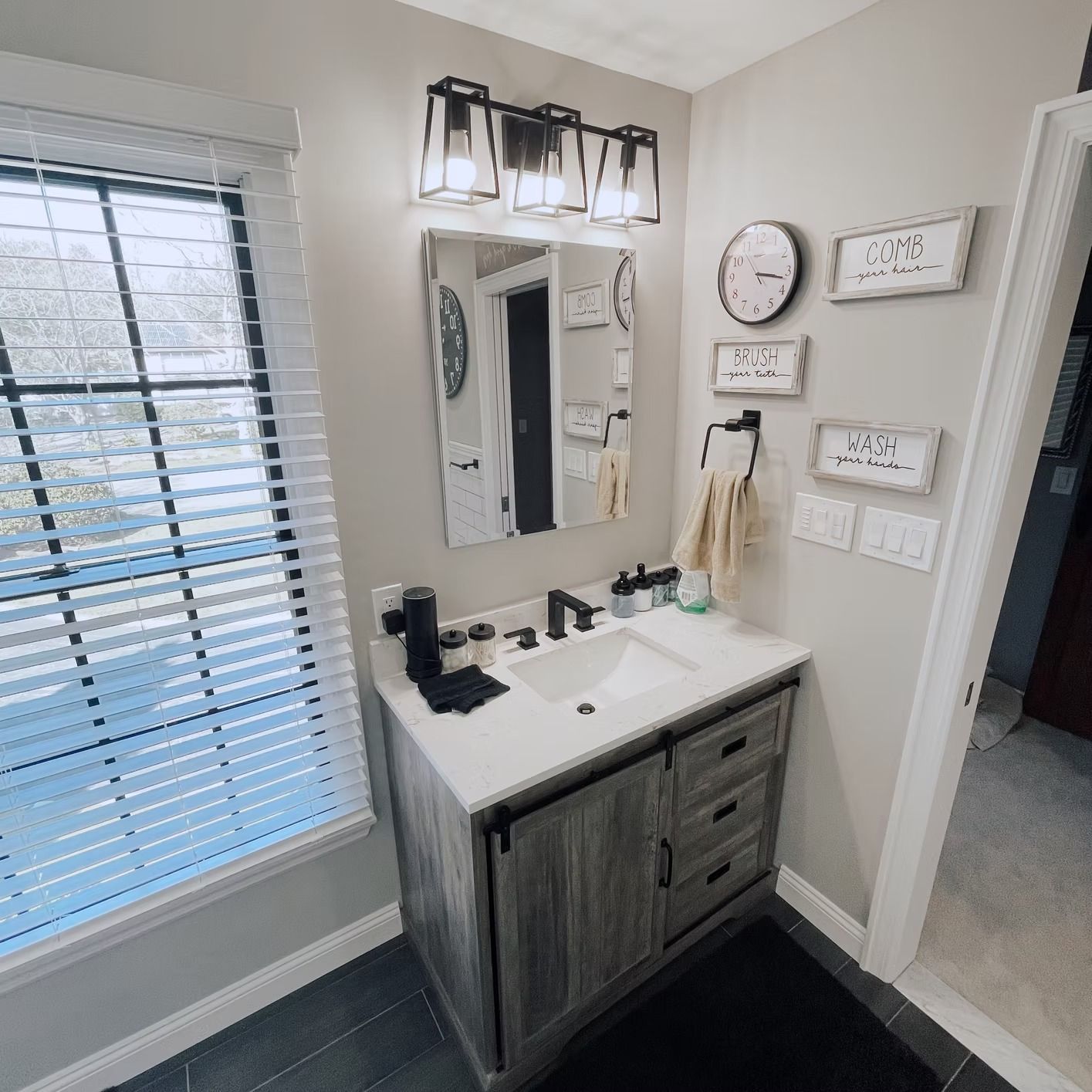 Bathroom with vanity, mirror, window, and wall decor. Gray and white color scheme.