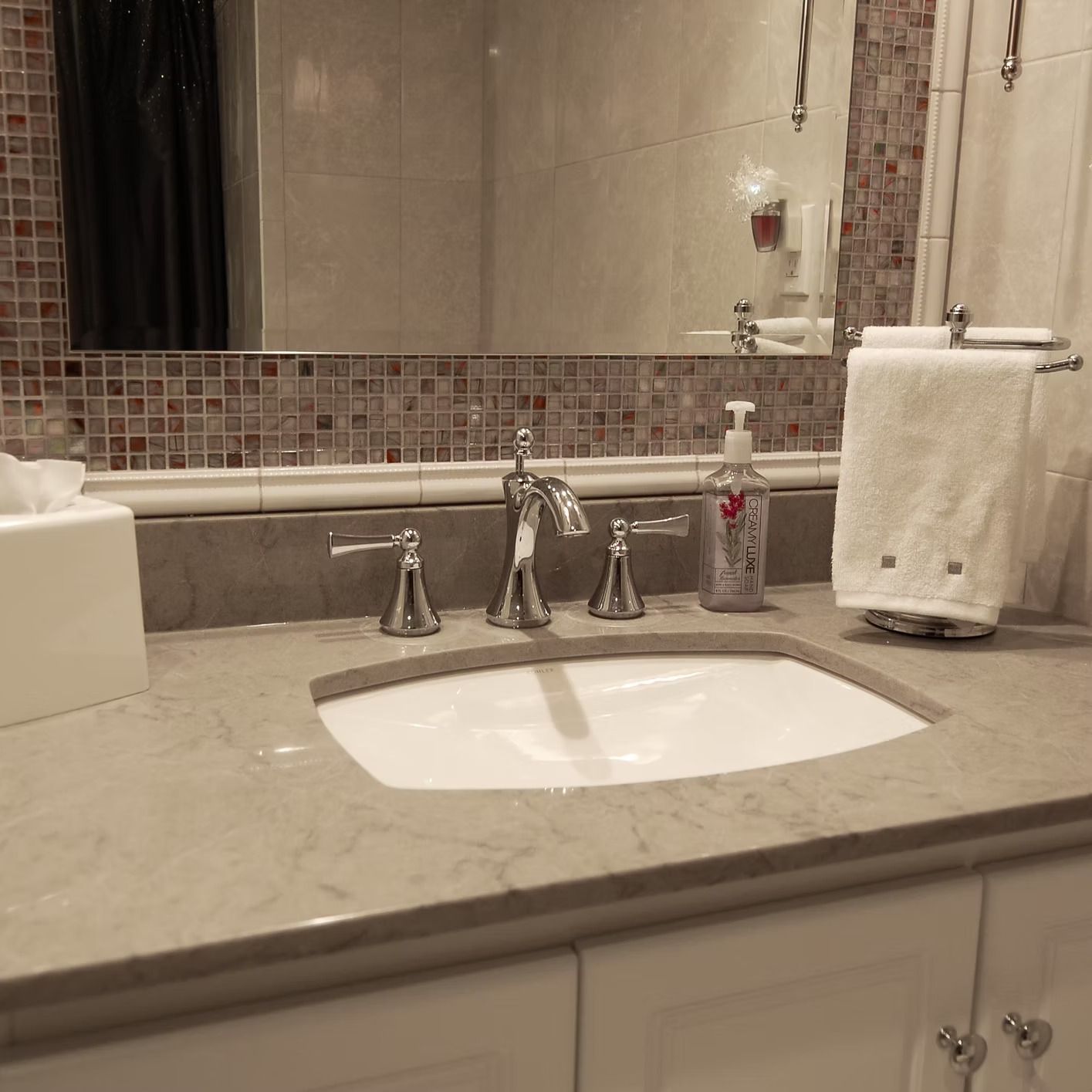 Bathroom vanity with a sink, mirror, and towels, featuring white cabinets and a light marble countertop.