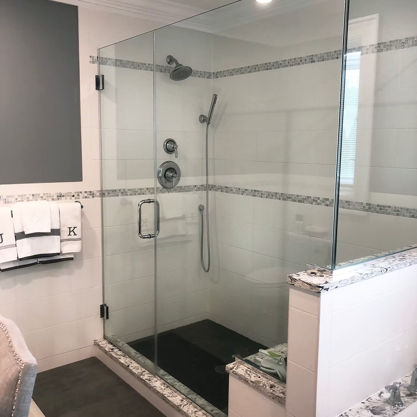 Glass shower enclosure with white tile and decorative trim.