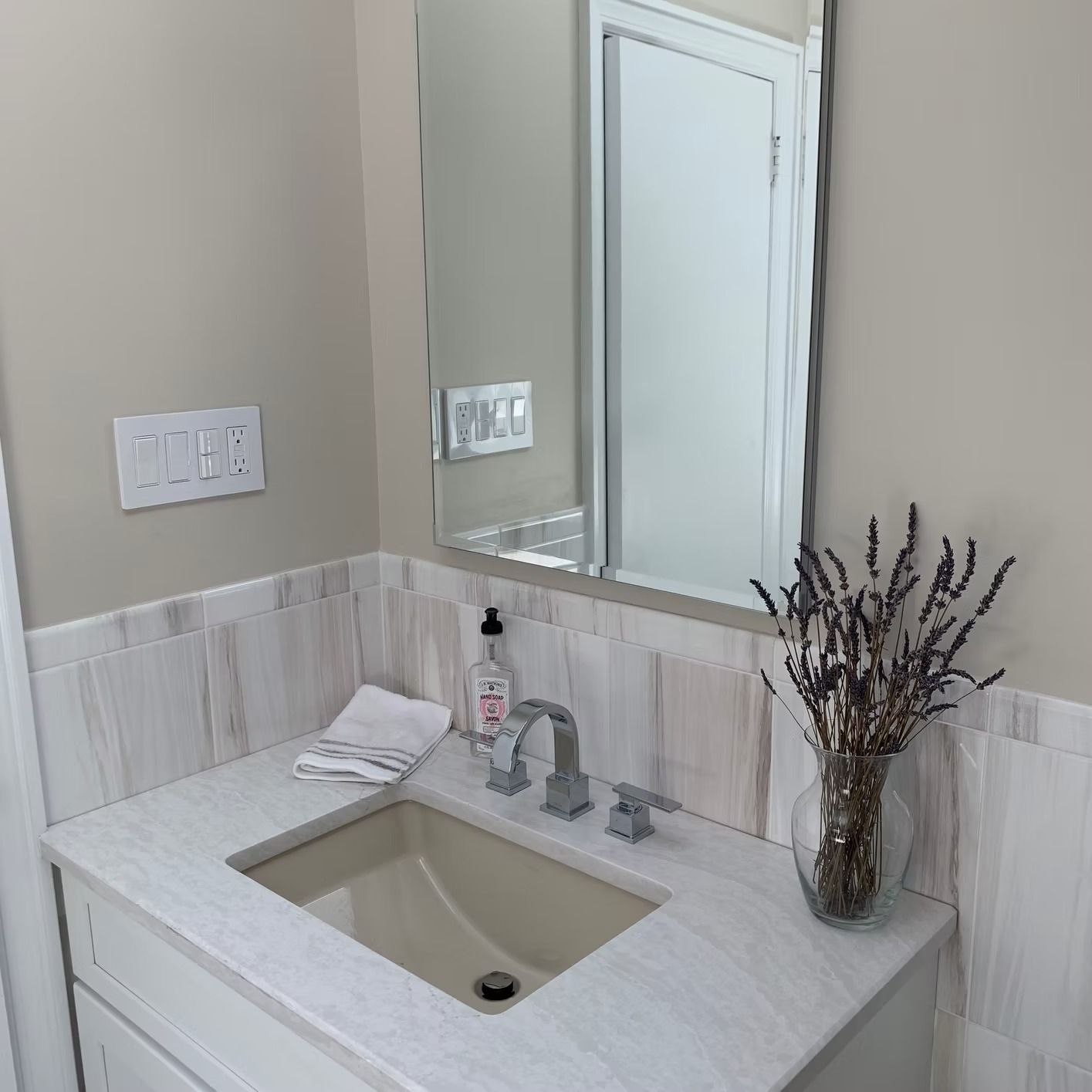 Bathroom vanity with a pale stone countertop, a square sink, mirror, and lavender.