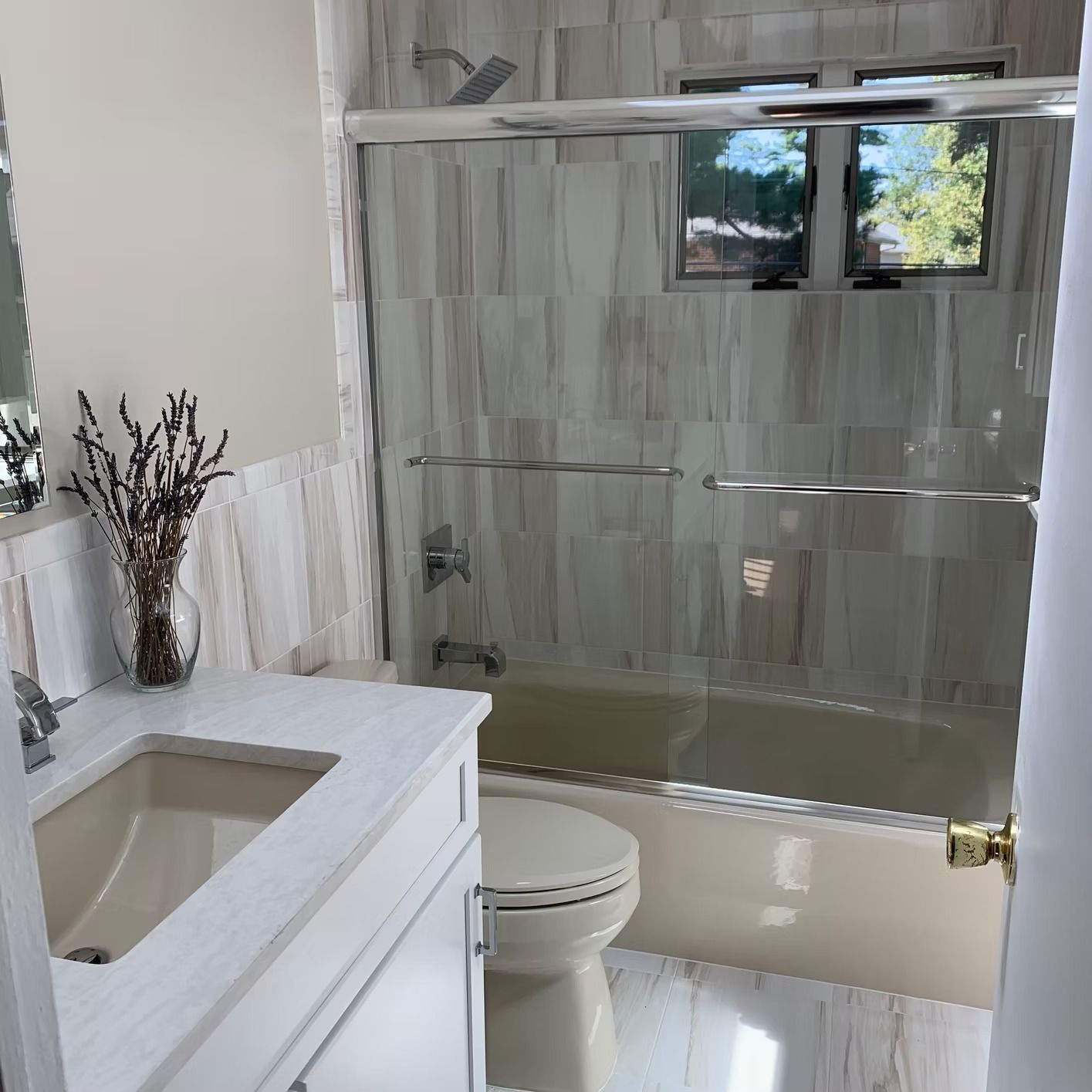 Bathroom with white marble tile, bathtub, toilet, and vanity. Dried flowers on the counter.