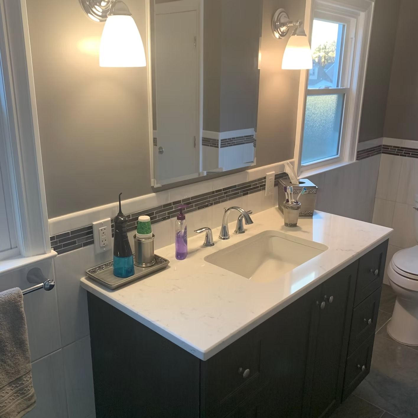 Bathroom with dark cabinets, white countertop, and gray walls, featuring a sink, mirror, and toiletries.