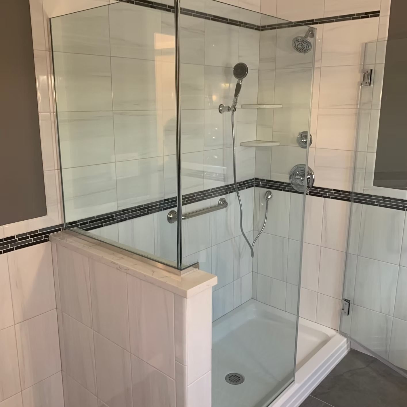 A modern glass shower with white tile walls and chrome fixtures, including a hand-held shower.