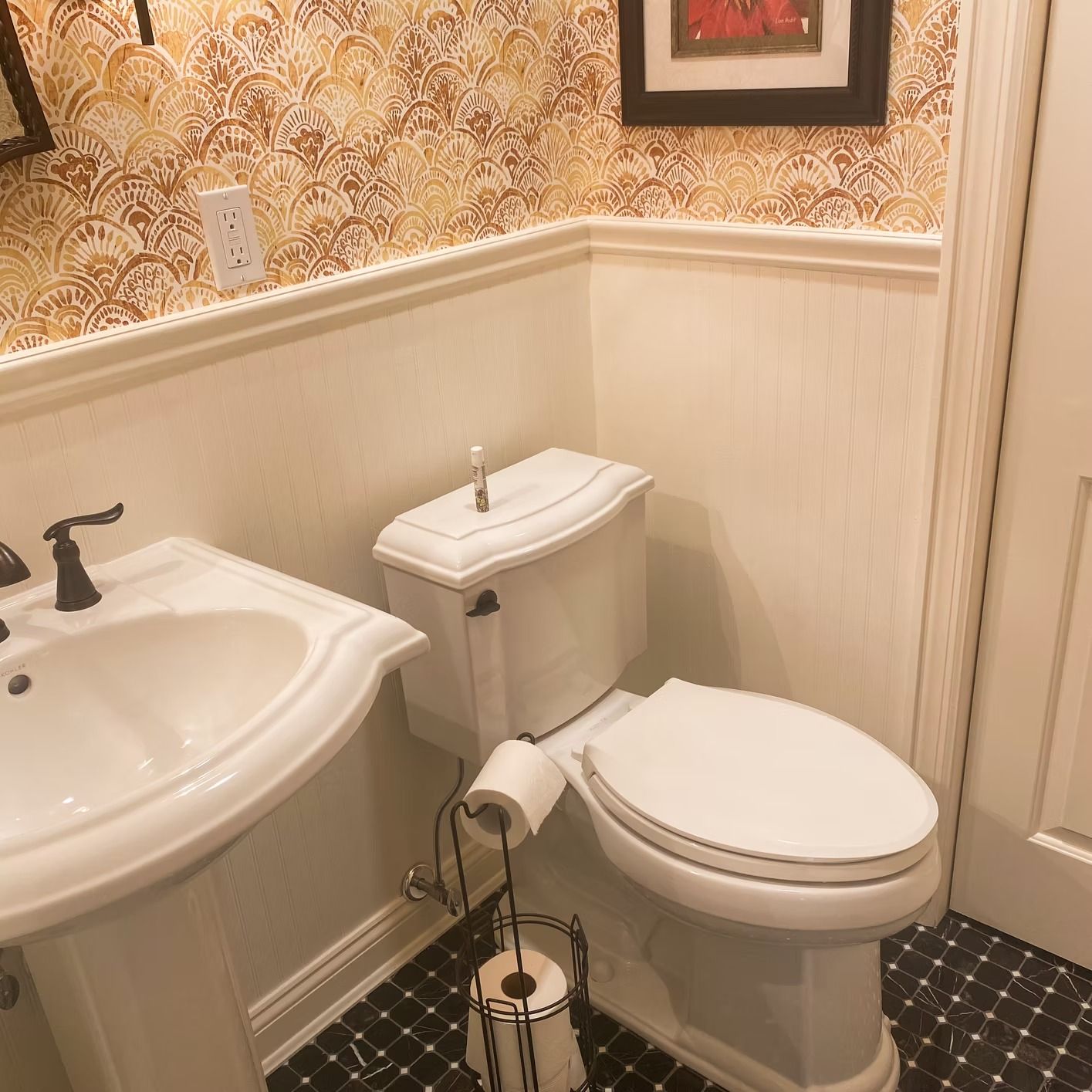 Bathroom with pedestal sink, toilet, patterned wallpaper, and black tiled floor.