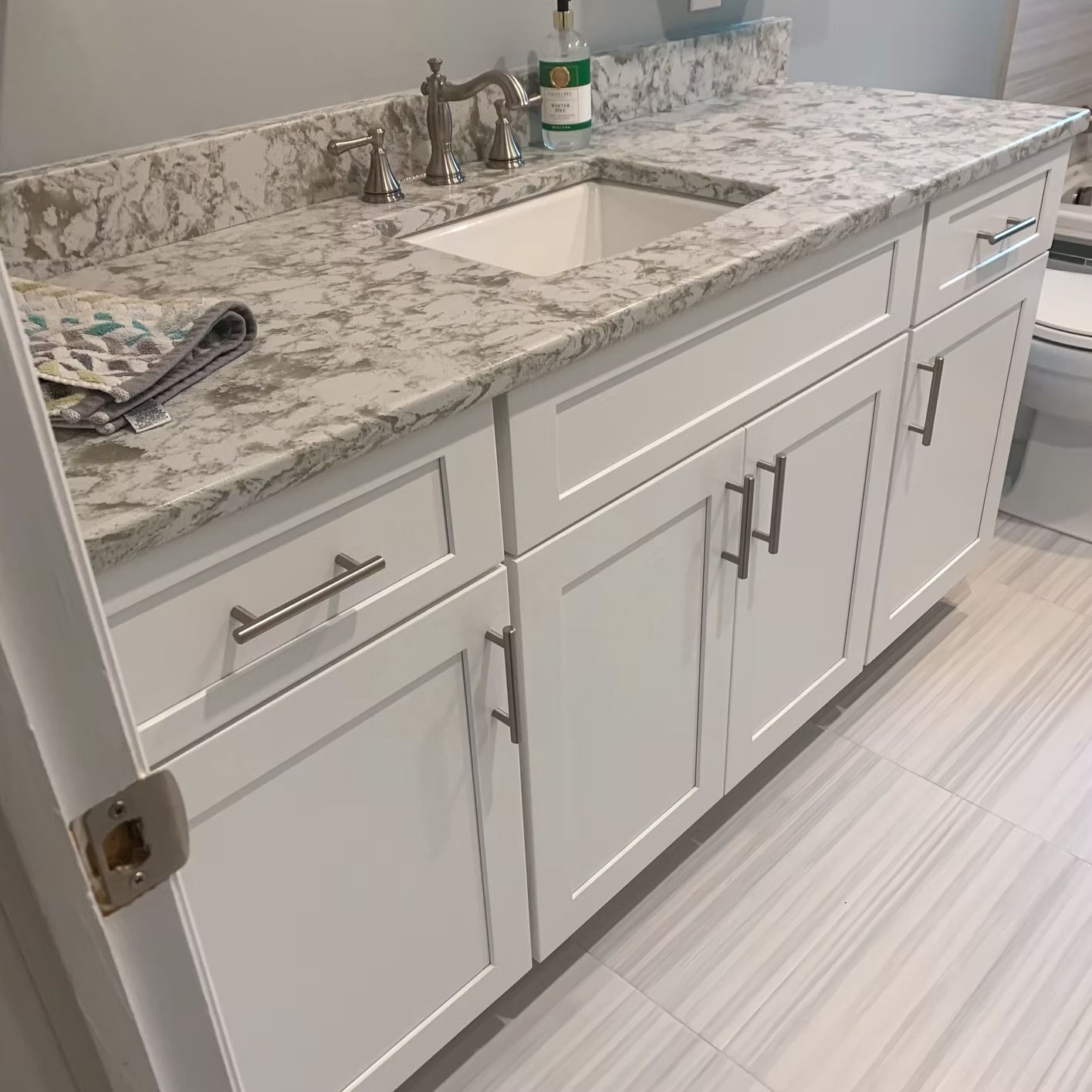 White bathroom vanity with marble countertop and silver fixtures, next to a toilet.