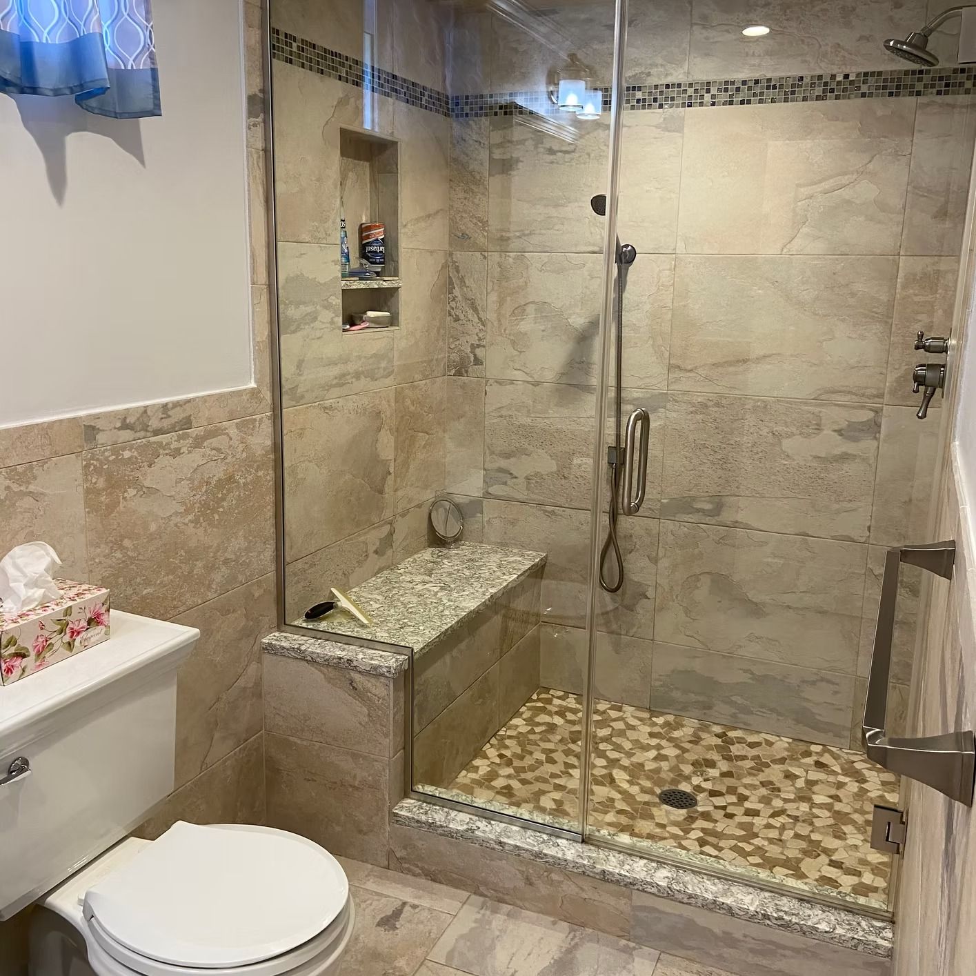 Bathroom with a glass shower, stone tile, a built-in bench, and a toilet.