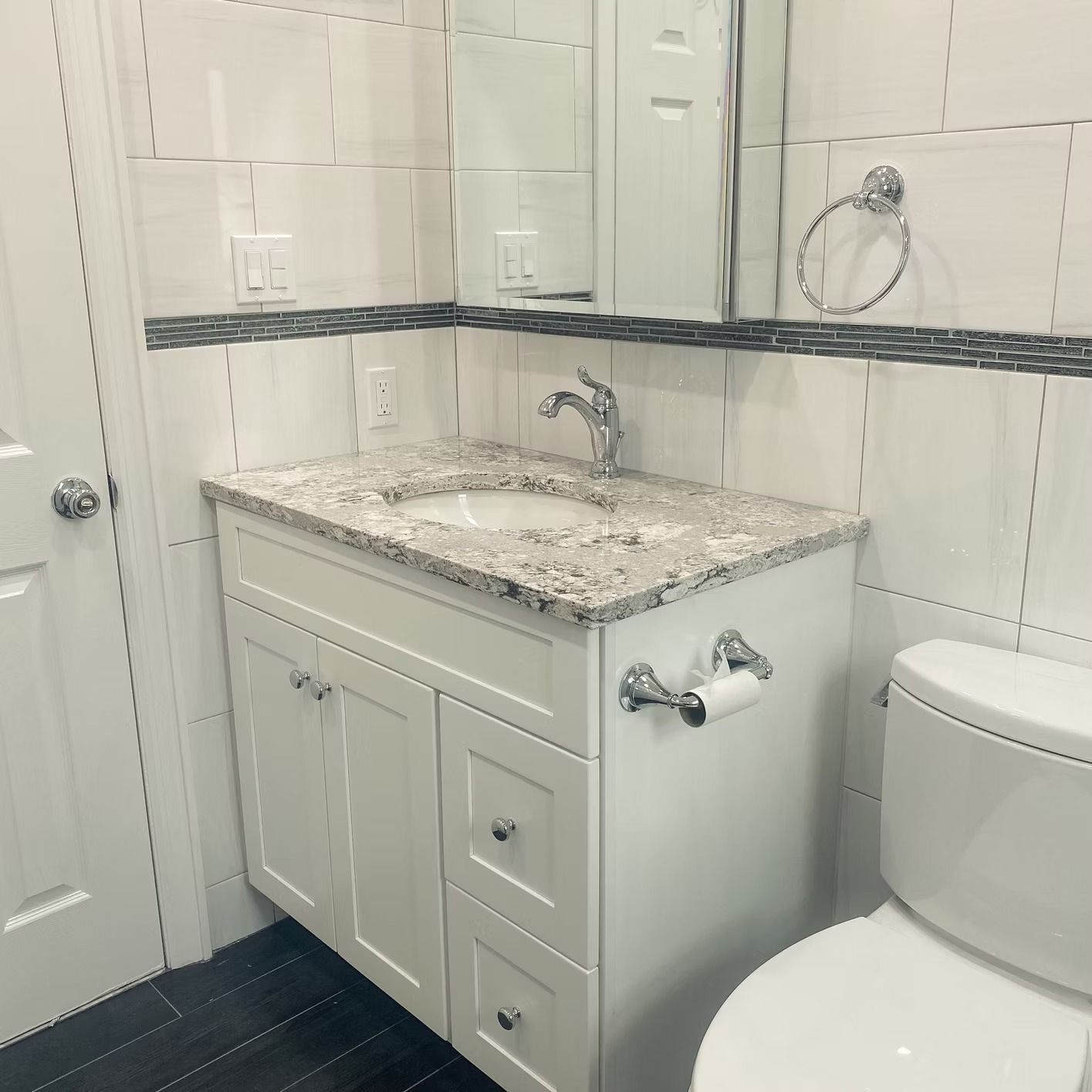White bathroom with sink, granite countertop, toilet, mirror, and white tile.
