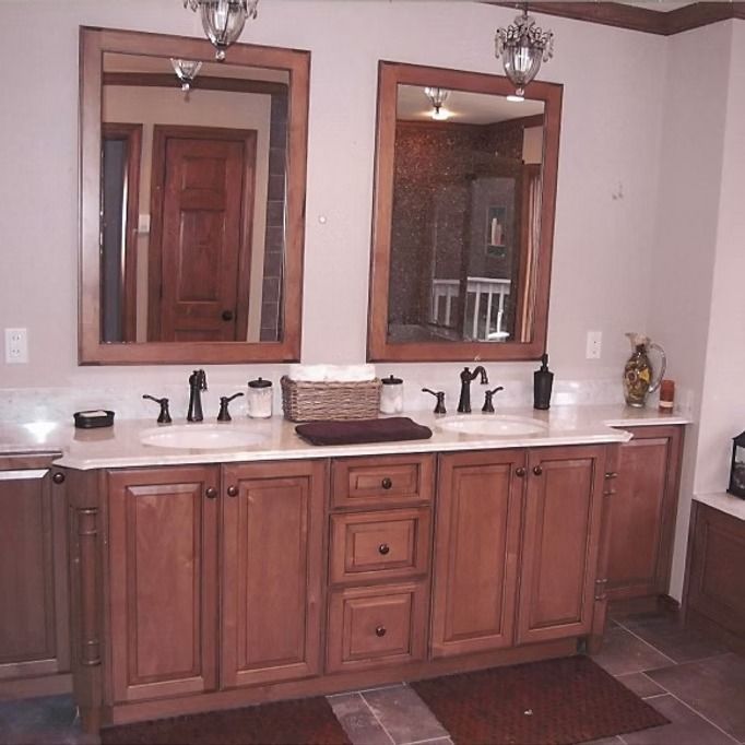 Bathroom with double sink vanity, brown cabinets, framed mirrors, and ornate light fixtures.