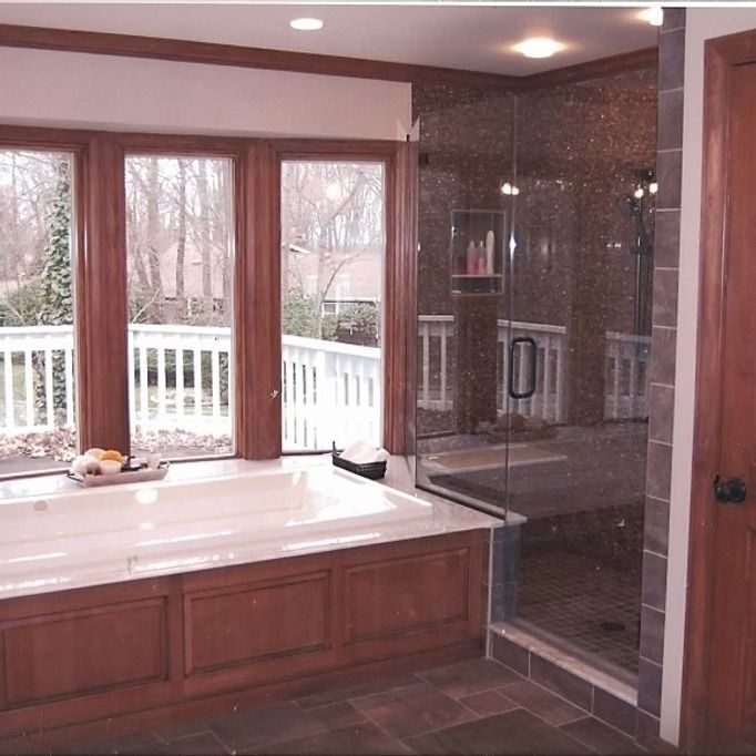 Bathroom with a soaking tub by a window, a glass shower, and wood trim.