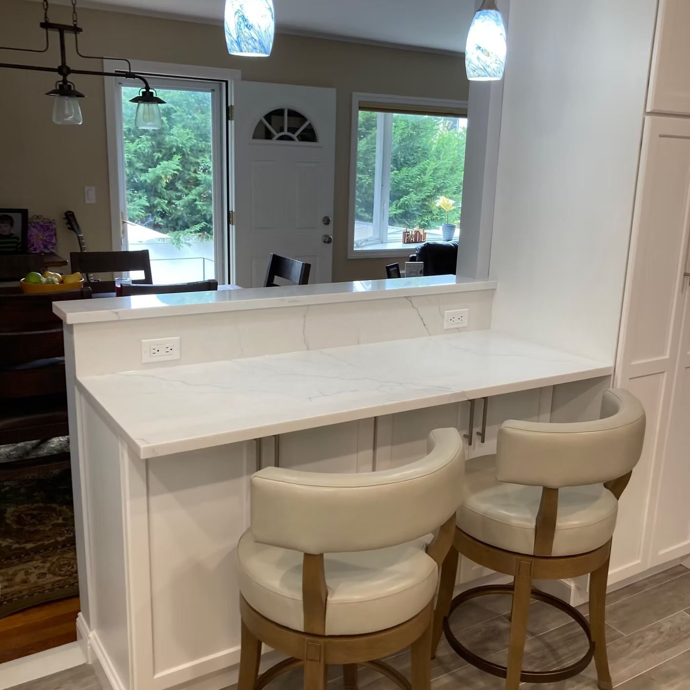 A kitchen bar with two cream-colored stools. White countertop and cabinets, with blue pendant lights.