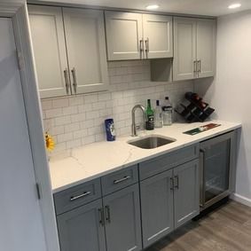 Gray and white bar area with cabinets, sink, and mini-fridge.