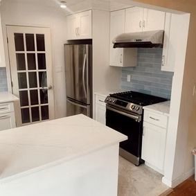 Kitchen remodel with white cabinets, stainless steel appliances, and a blue backsplash.