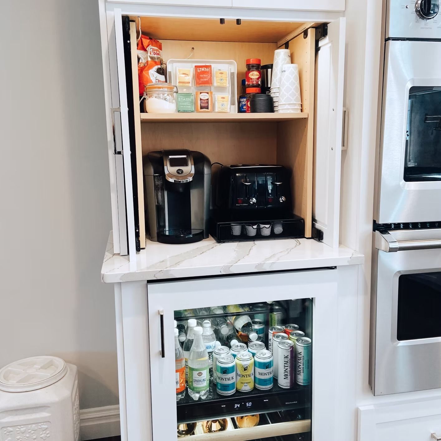 Built-in kitchen cabinet with coffee maker, toaster, and beverage cooler. White cabinets with stainless steel appliances.