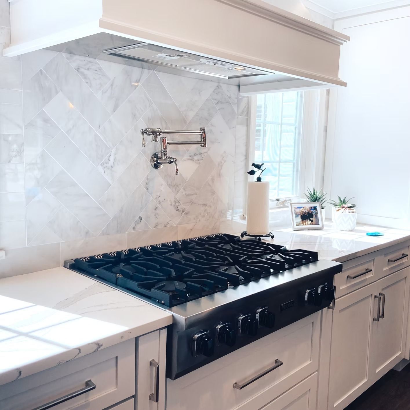 White kitchen with marble backsplash, stainless steel stove, and white cabinets.