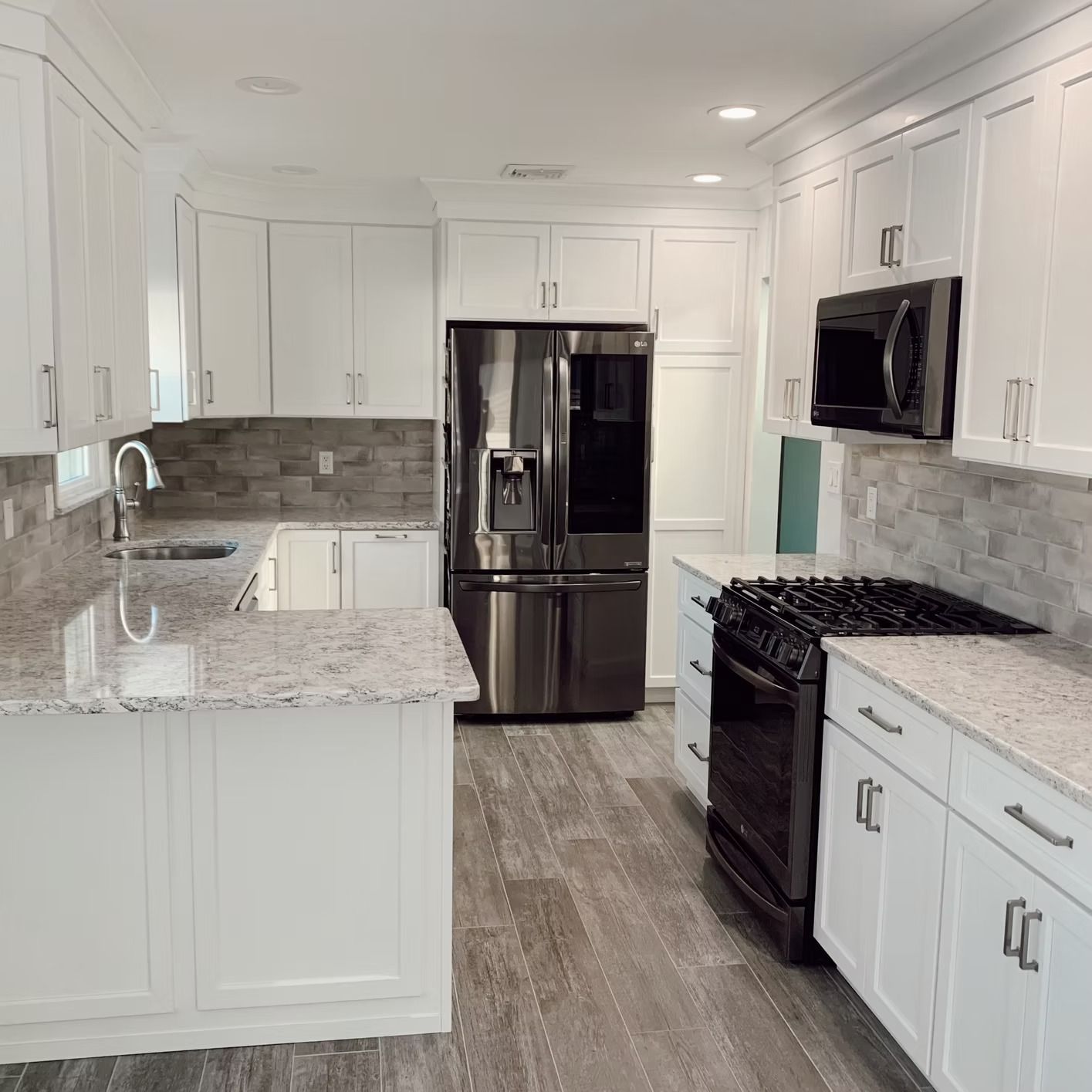 White kitchen with stainless steel appliances, granite countertops, and gray backsplash and flooring.