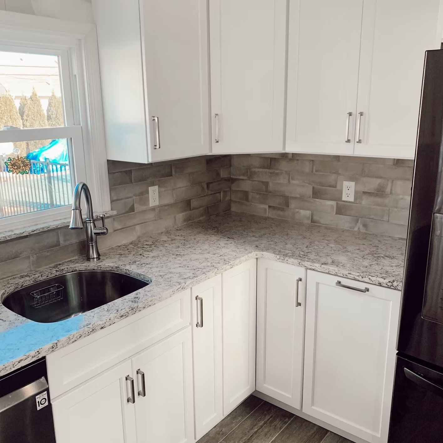 White kitchen with granite countertops, stainless steel sink, and gray brick backsplash.