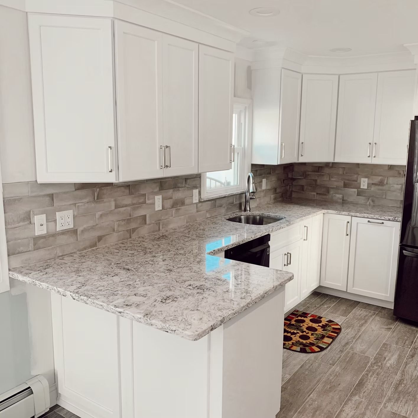 White kitchen cabinets with granite countertops. Grey stone backsplash and stainless steel sink.