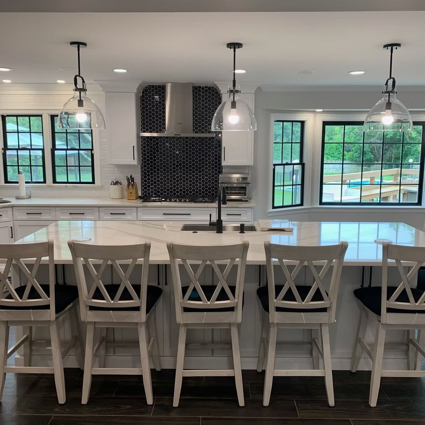 White kitchen with island, black windows, and pendant lights.