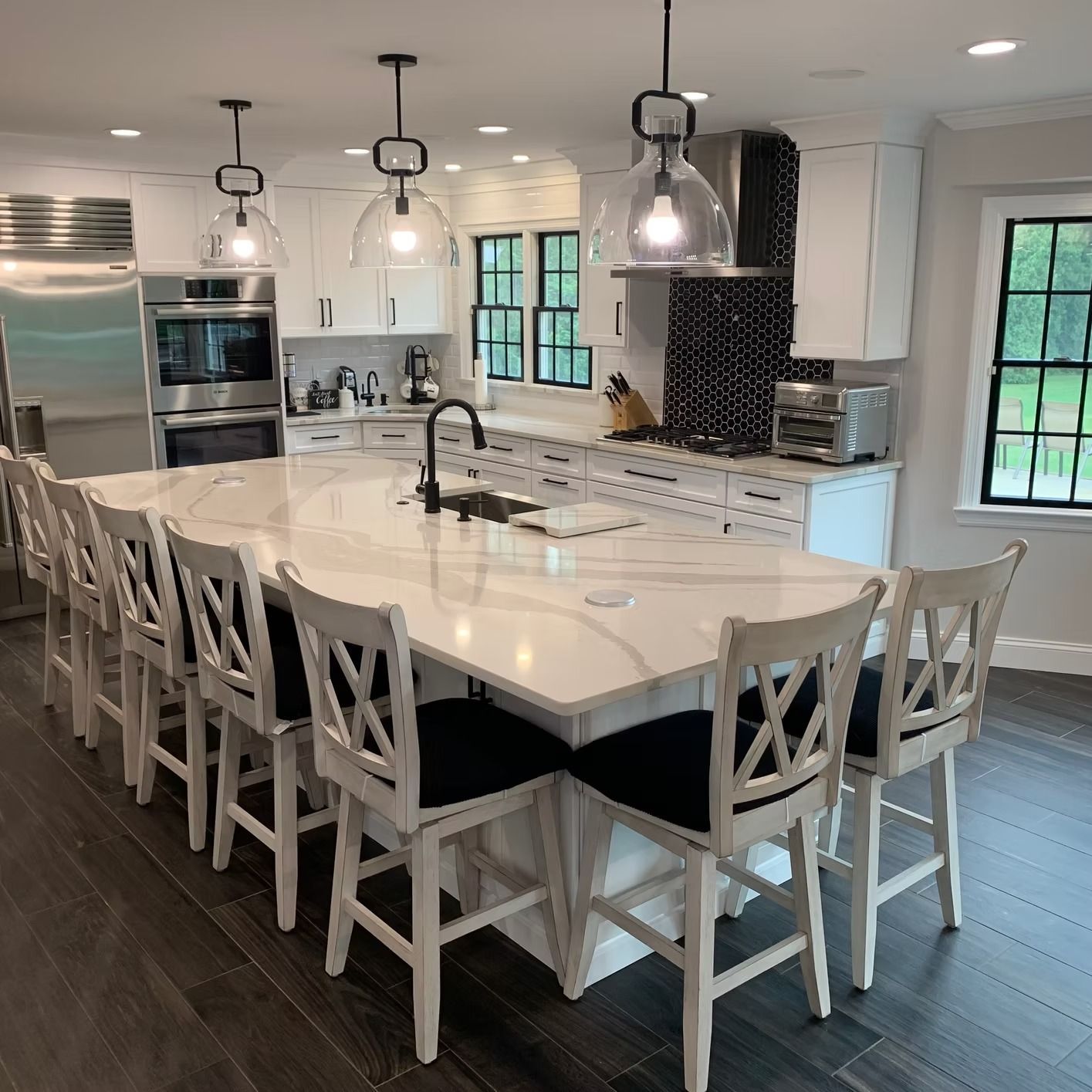 Spacious white kitchen with large island, seating, and pendant lights. Black and white accents.
