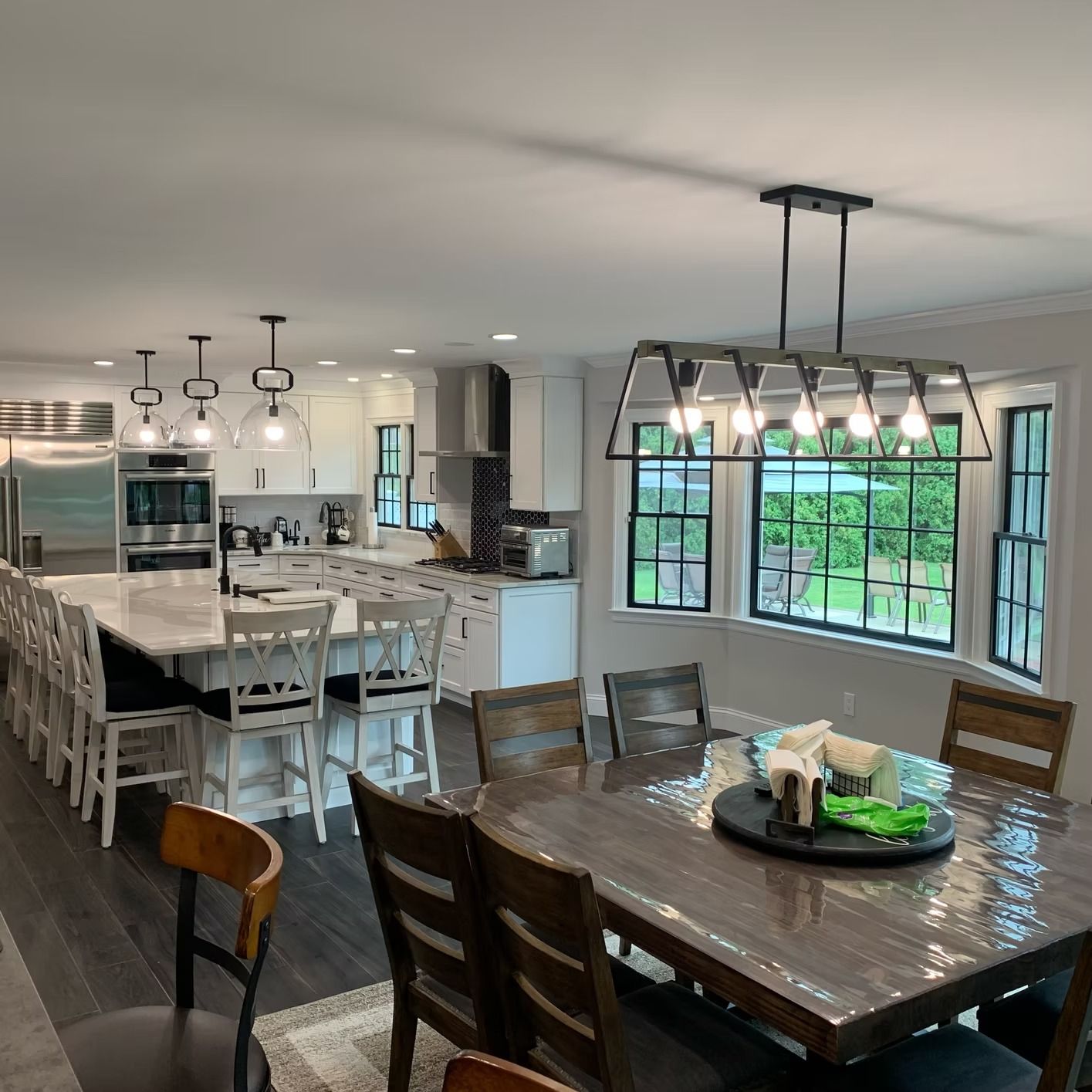 Open-plan kitchen and dining area with island seating, a long table, and large windows.