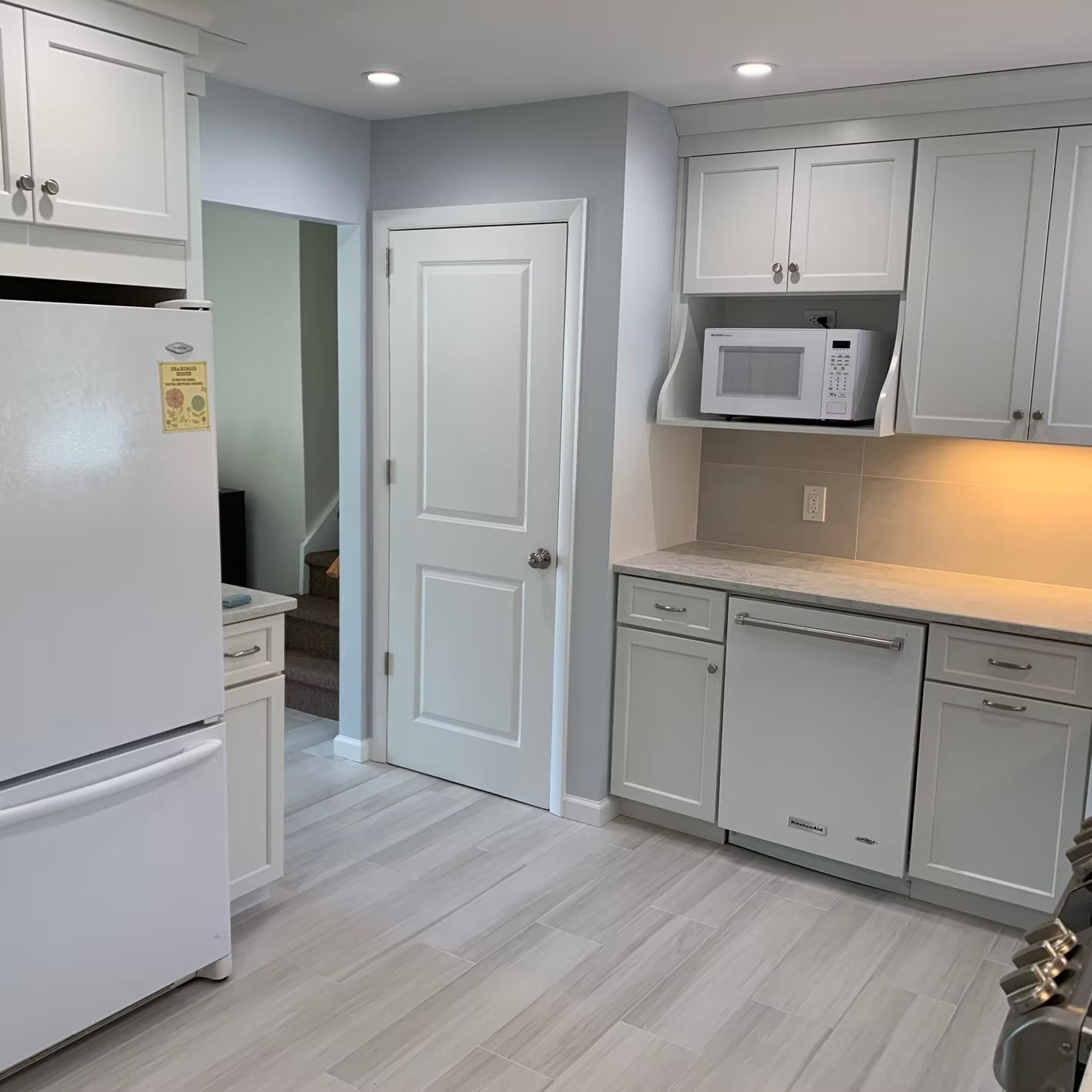 White kitchen with cabinets, appliances, light blue walls, and light gray flooring.
