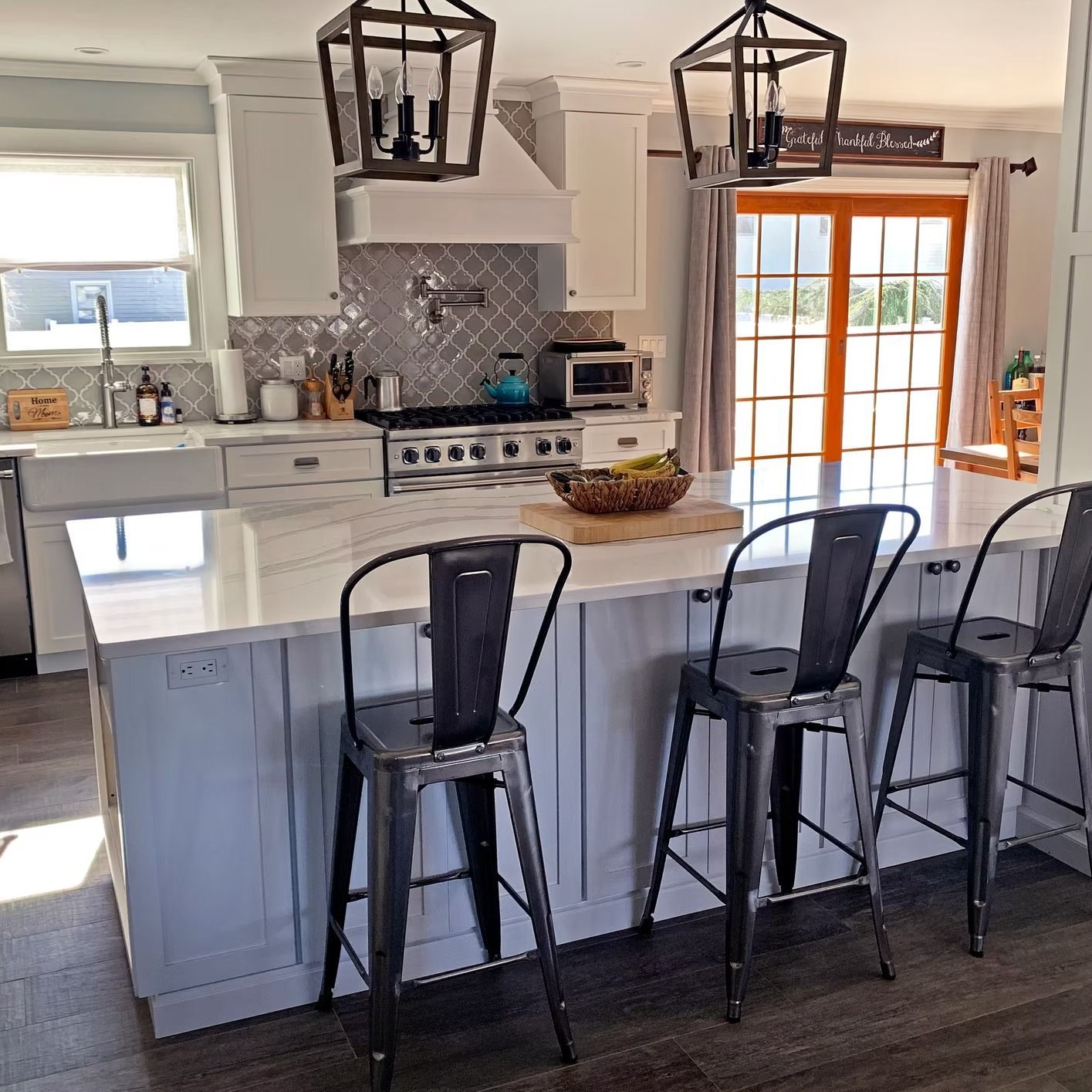 Kitchen with island, three bar stools, pendant lights, and stainless steel appliances.