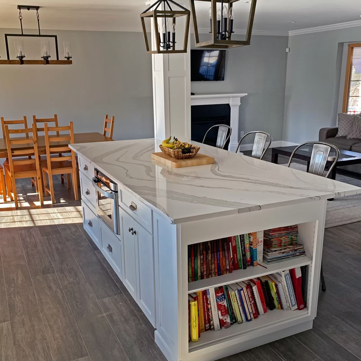 White kitchen island with quartz countertop, a bookcase, and built-in oven.