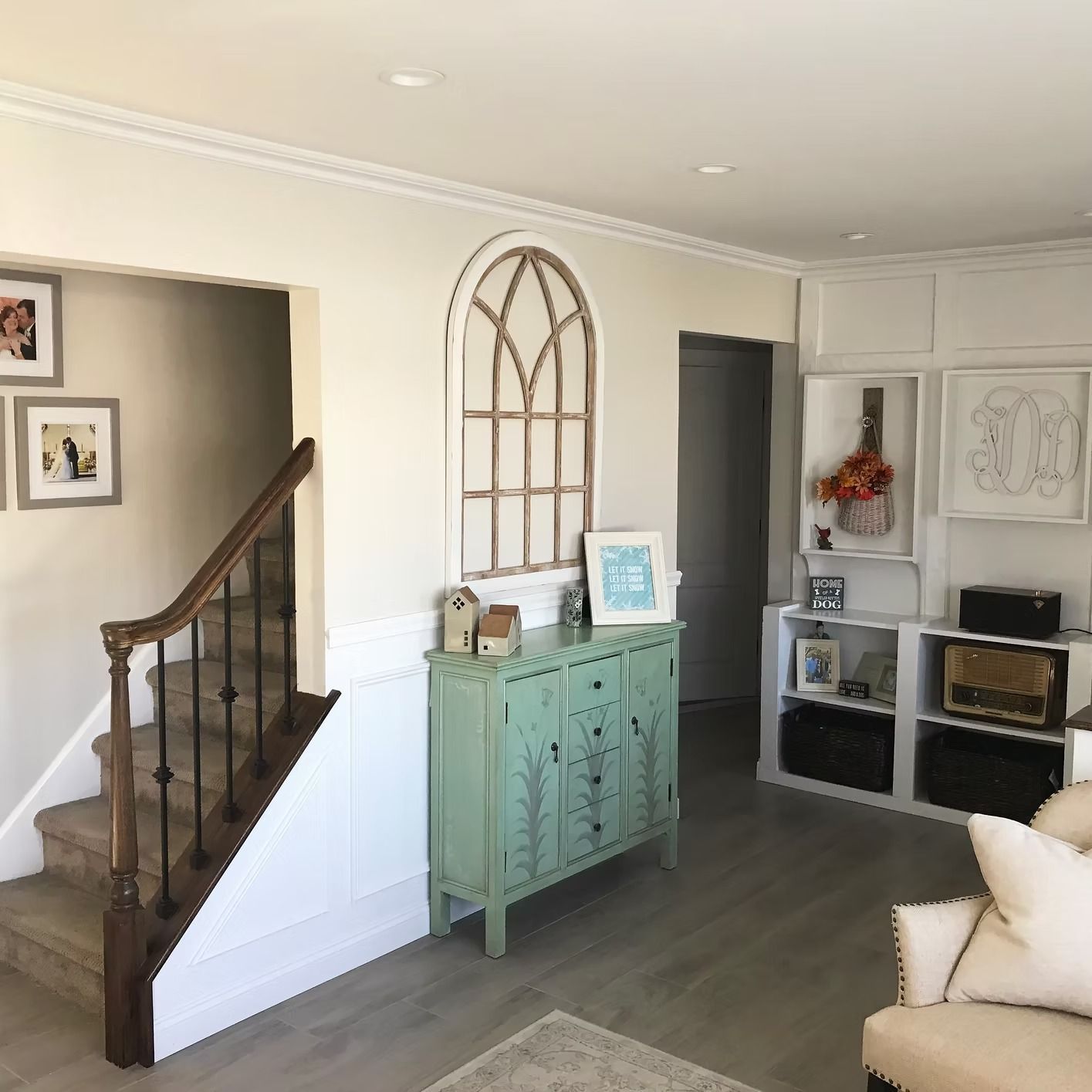 Living room with staircase, teal cabinet, and wooden-framed art on a cream-colored wall.