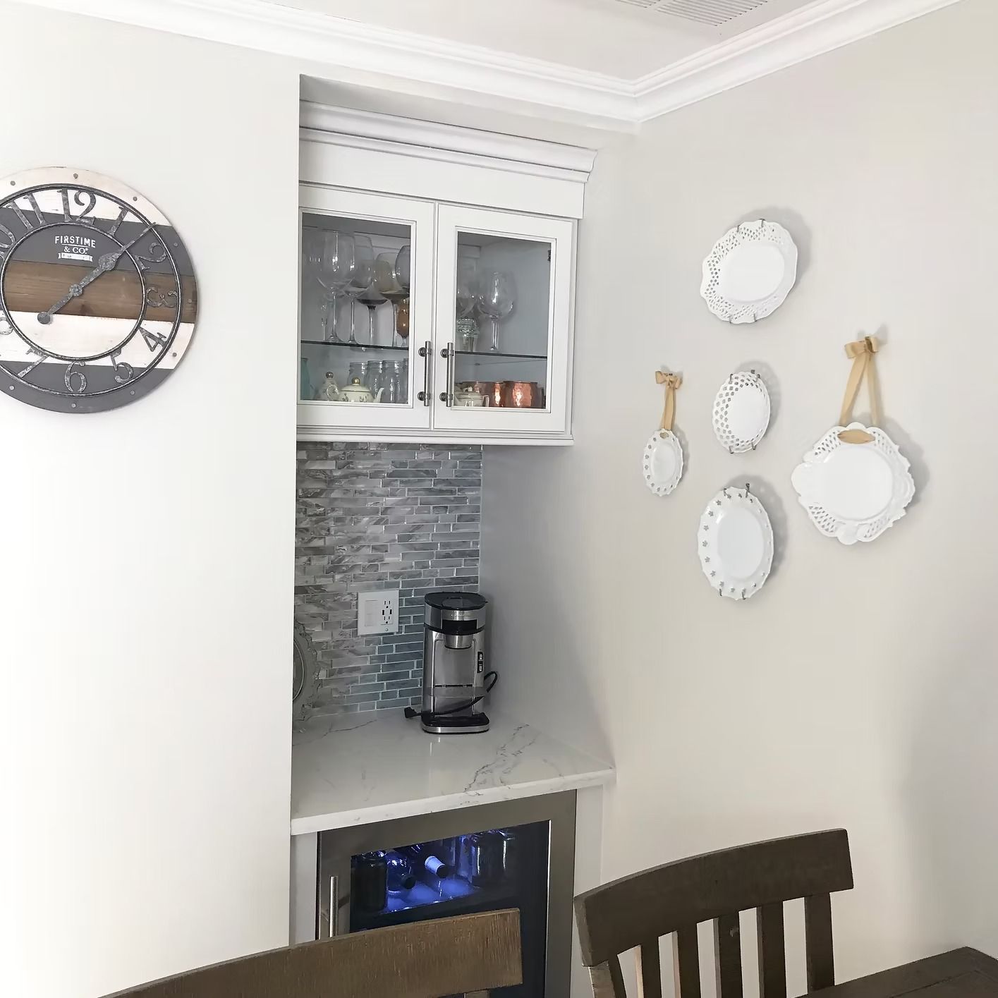 Built-in coffee station in a corner with a clock, white cabinet, tiled backsplash, and decorative plates.