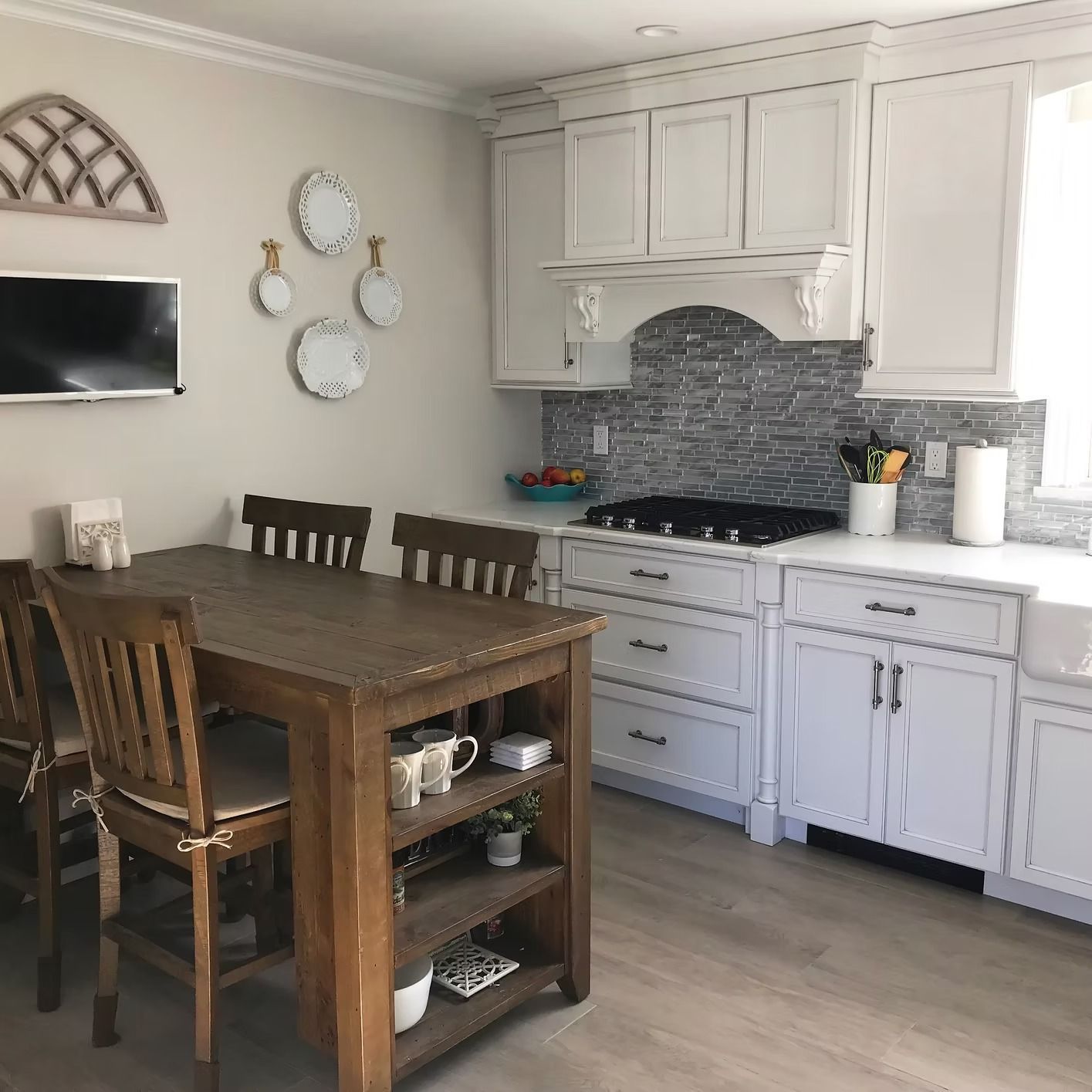 Kitchen with white cabinets, gray backsplash, wooden table with chairs, and a mounted TV.