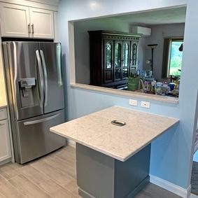 Kitchen with stainless steel refrigerator, gray cabinets, and a counter with a pass-through to another room.