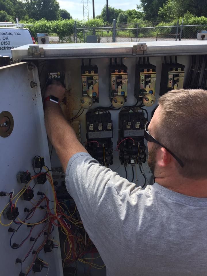 An electrician works inside an open outdoor electrical control panel, adjusting components with their hand.